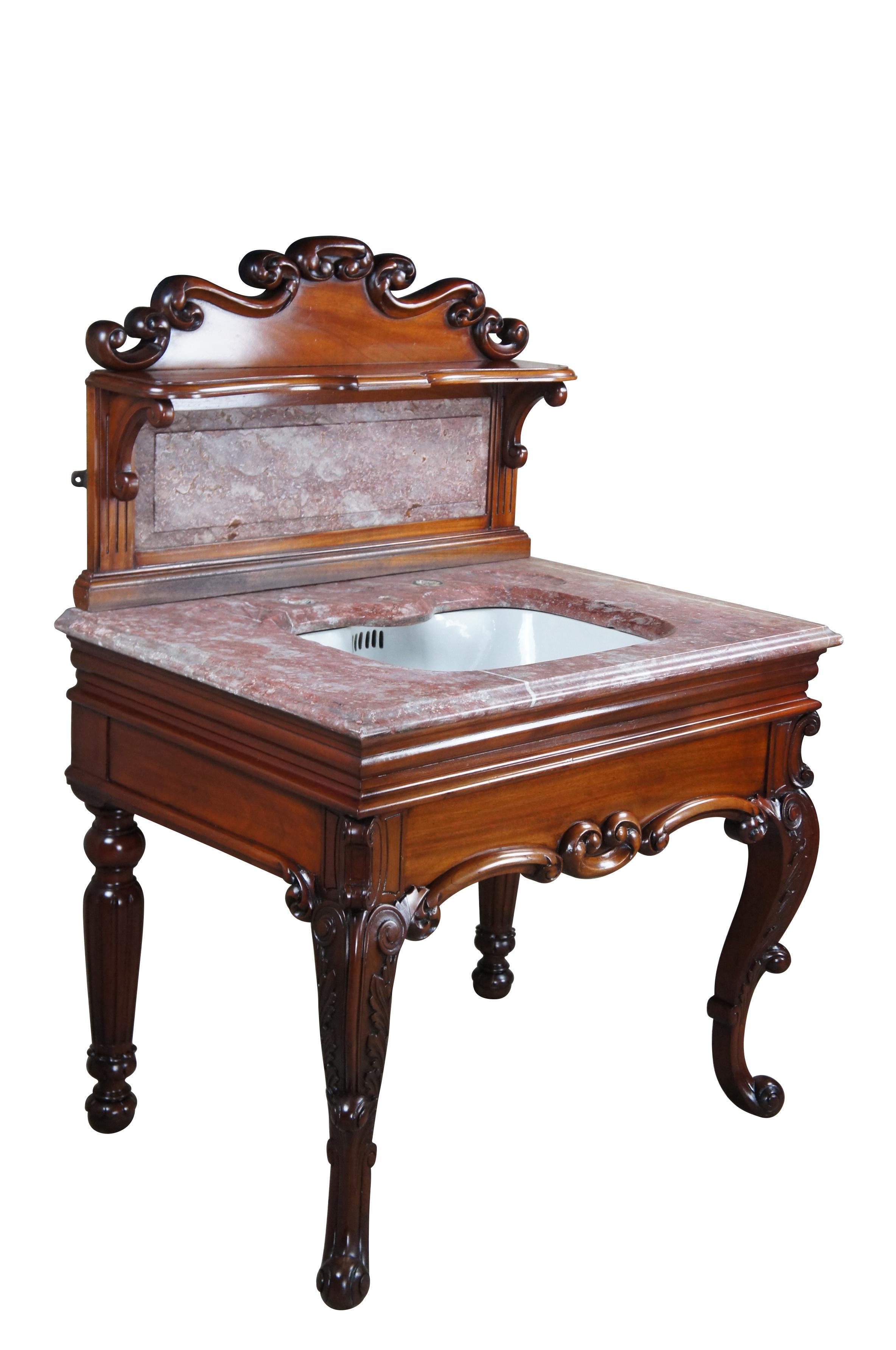 An exquisite Victorian Era bathroom vanity.  Features a red and white vein marble top with scalloped soap holders and porcelain sink basins by John Shanks (Britain).  The spectacular mahogany base features  