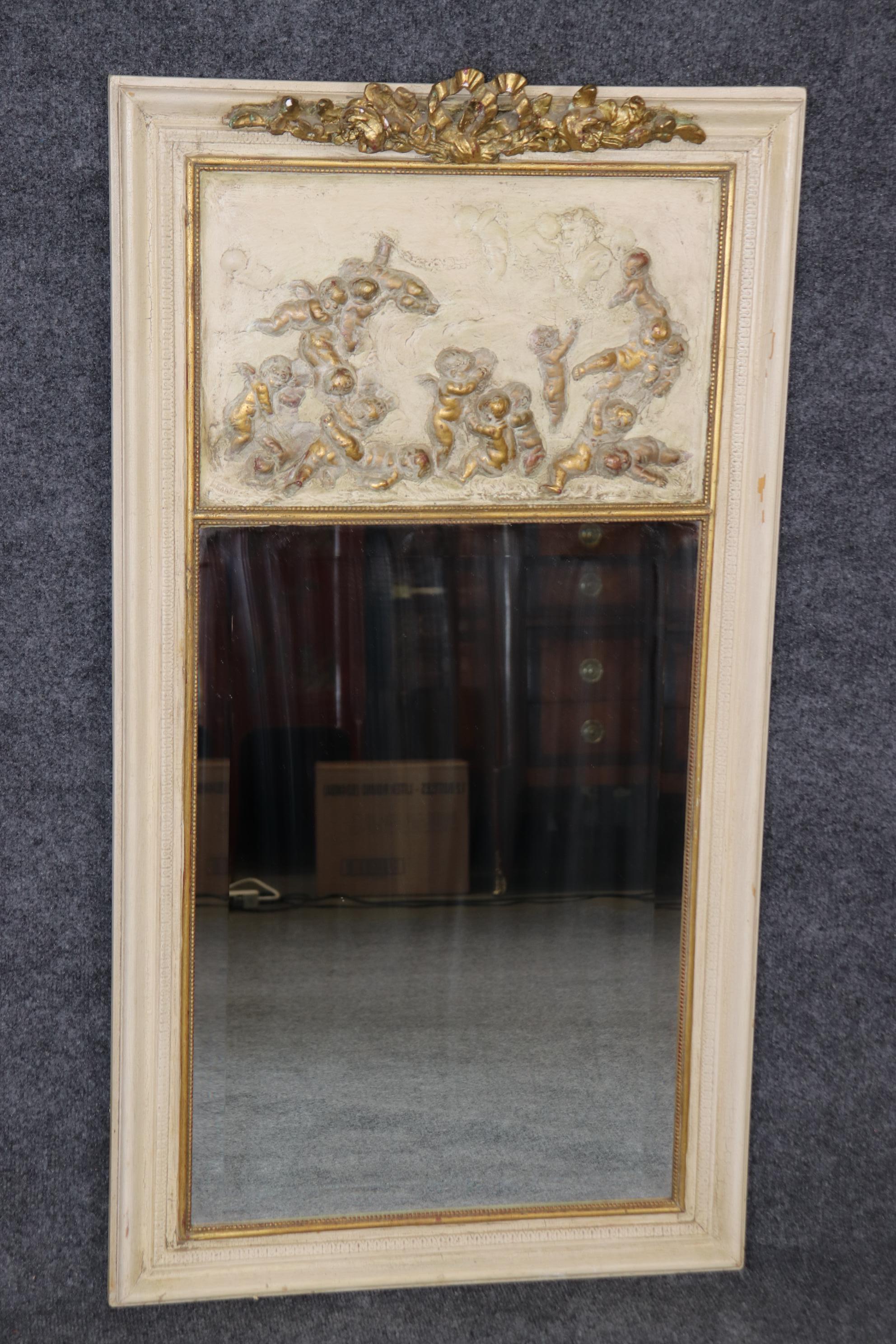 This is a gorgeous French 1900s era cherub or putti mirror with numerous cherubs playing together on a creme painted background with genuine gold leaf details. The mirror is made of pine which is unusual and shows a primitive yet very well-executed