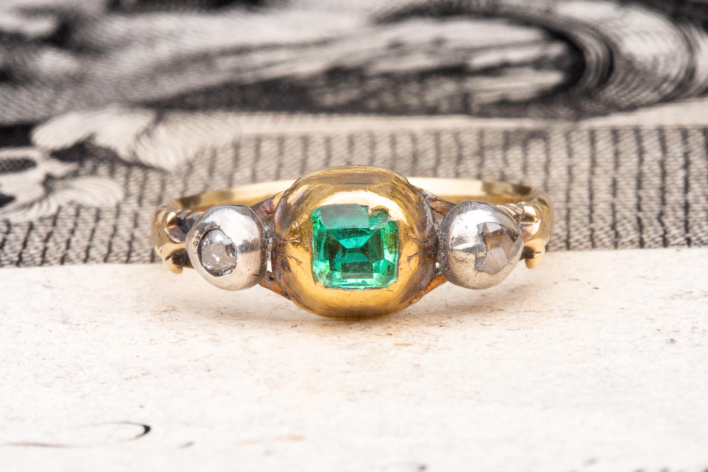 This outstanding gold three stone ring dates to around 1790 and was made in Western Europe. A table cut natural emerald, likely to be of Columbian origin, is mounted in a rub-over setting and displays a gorgeous bright green hue. 

It is flanked