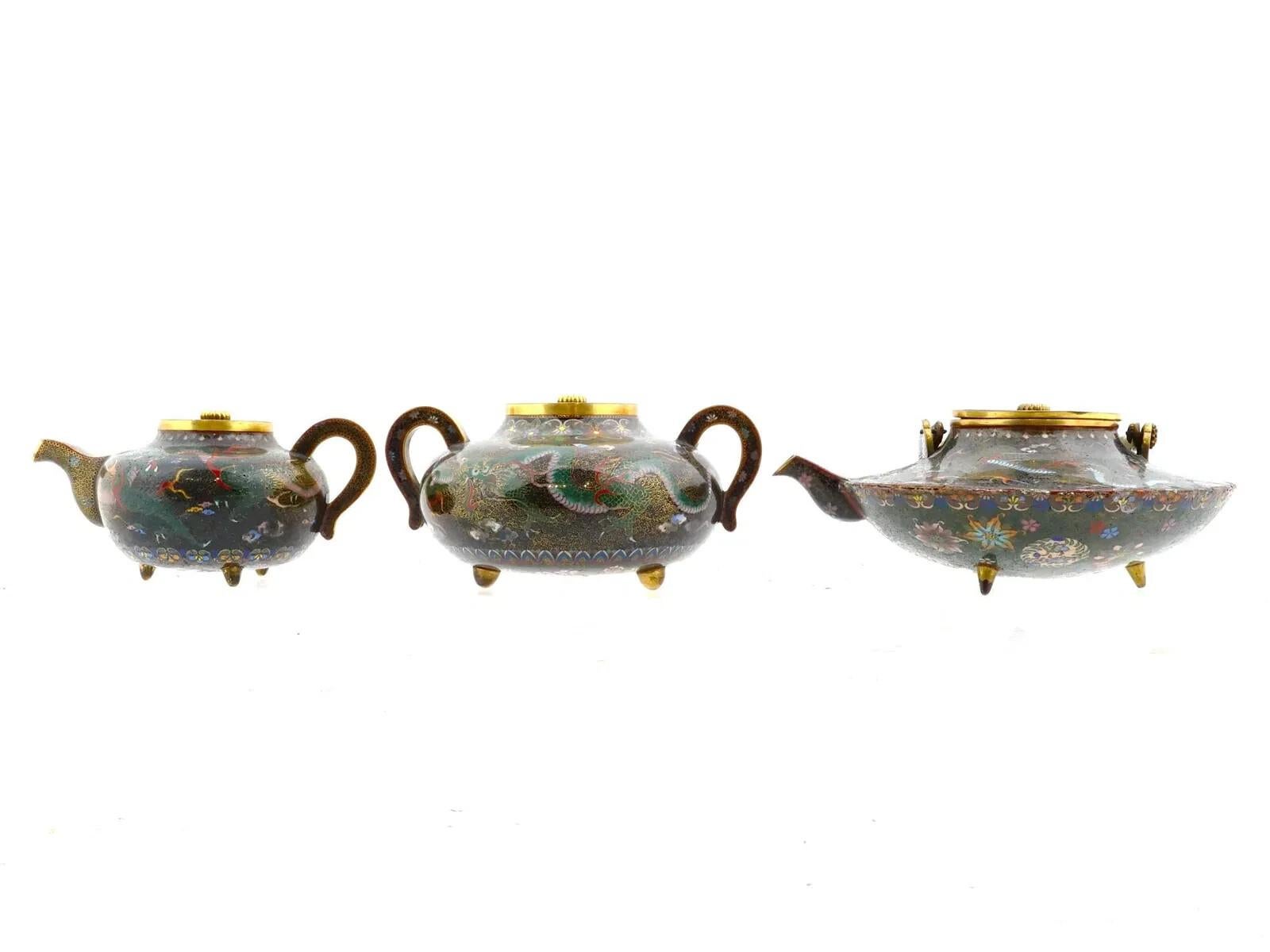 Juego de té japonés esmaltado con tapa y pie que incluye tres piezas. El juego incluye una tetera grande, una tetera pequeña y un azucarero. Las piezas están adornadas con un diseño de esmalte policromado que representa dragones rodeados de adornos
