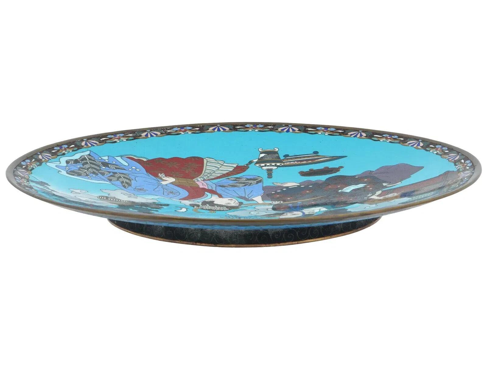 Antiguo plato japonés de cobre para servir con diseño de esmalte cloisonné policromado. Periodo Meiji, hacia la década de 1880. Pieza de pie redondo. Color de fondo azul turquesa. La placa representa a un samurai y una geisha en un paisaje. Borde