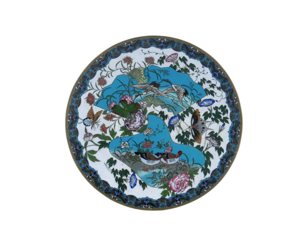 Un piatto decorativo in ottone di alta qualità dell'epoca Meiji giapponese, dal 1868 al 1912. Attribuito a GOTO

L'esterno del piatto è ornato da fiori policromi e farfalle su un fondo di smalto bianco e dipinto con le immagini di una coppia di gru