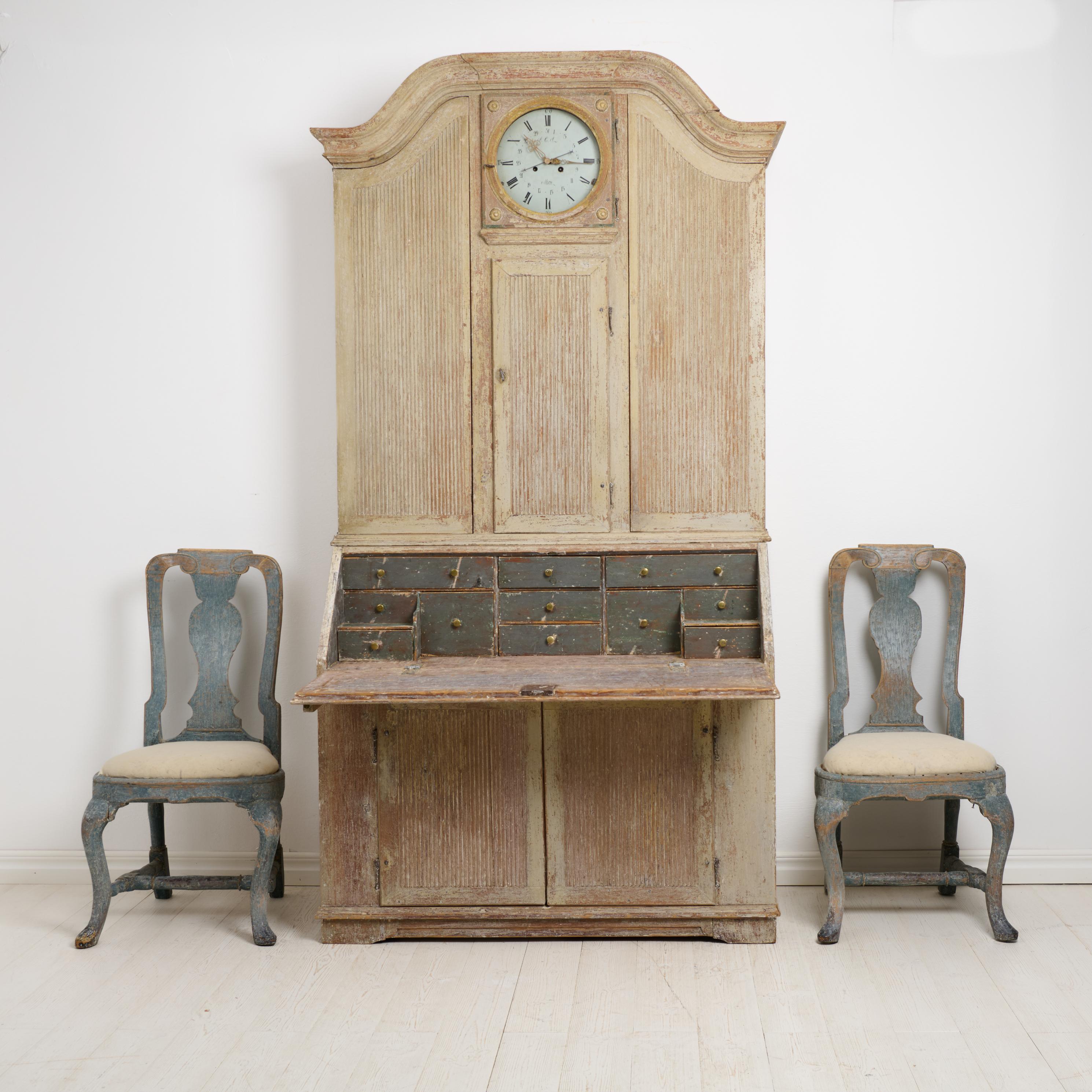 Rare Antique Secretary Cabinet in rococo with a clock. The cabinet is made by hand in solid pine around 1820 in northern Sweden. The cabinet is made in two parts. A lower cabinet with a secretary desk and interior drawers and an upper cabinet with a
