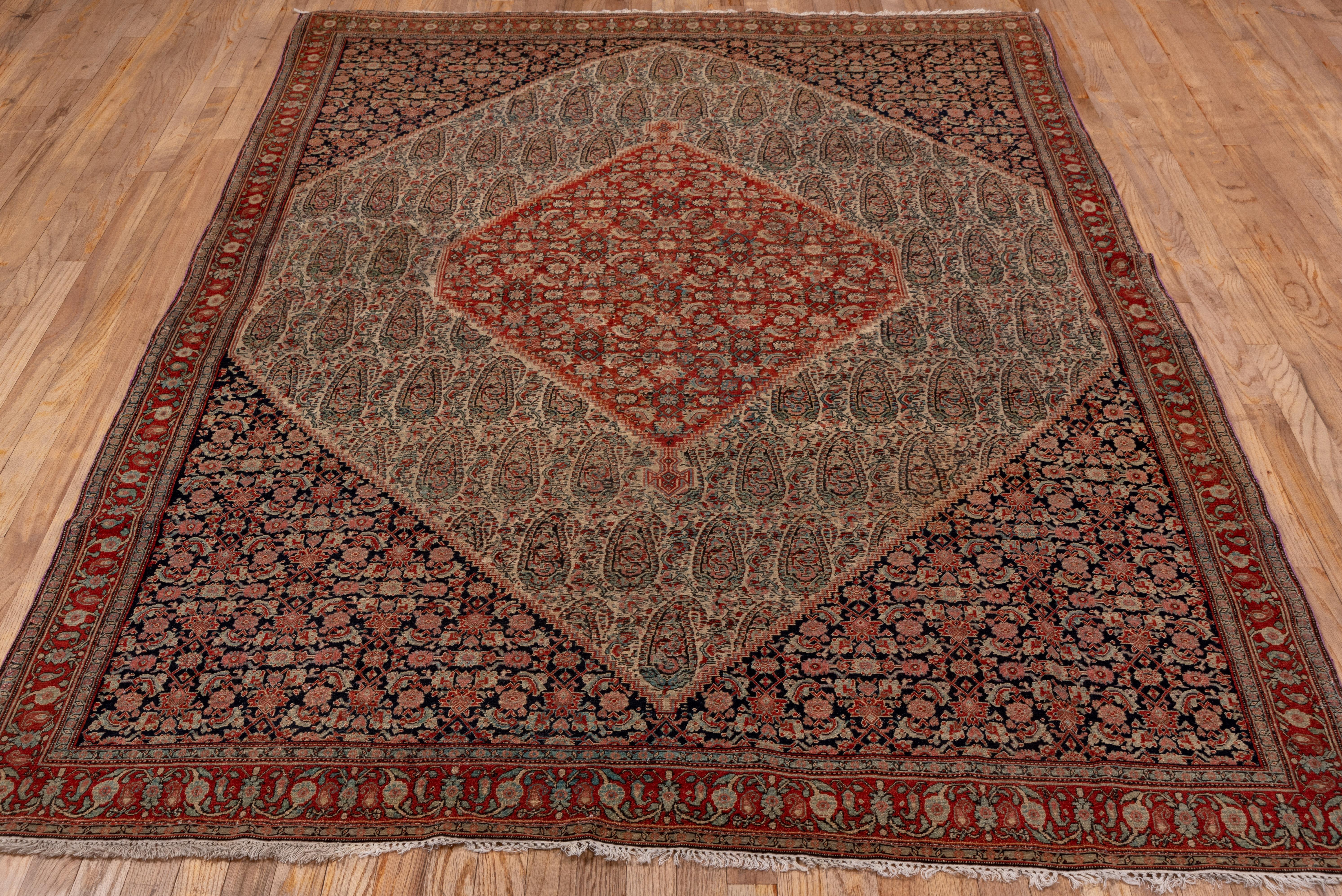 Larger than the usual Senneh scatter, this NW Persian finely woven Kurdish city rug shows an invariant Herati design in the red medallion and navy corners, with large complex botehs in the cream field between. Red rosette and boteh border.