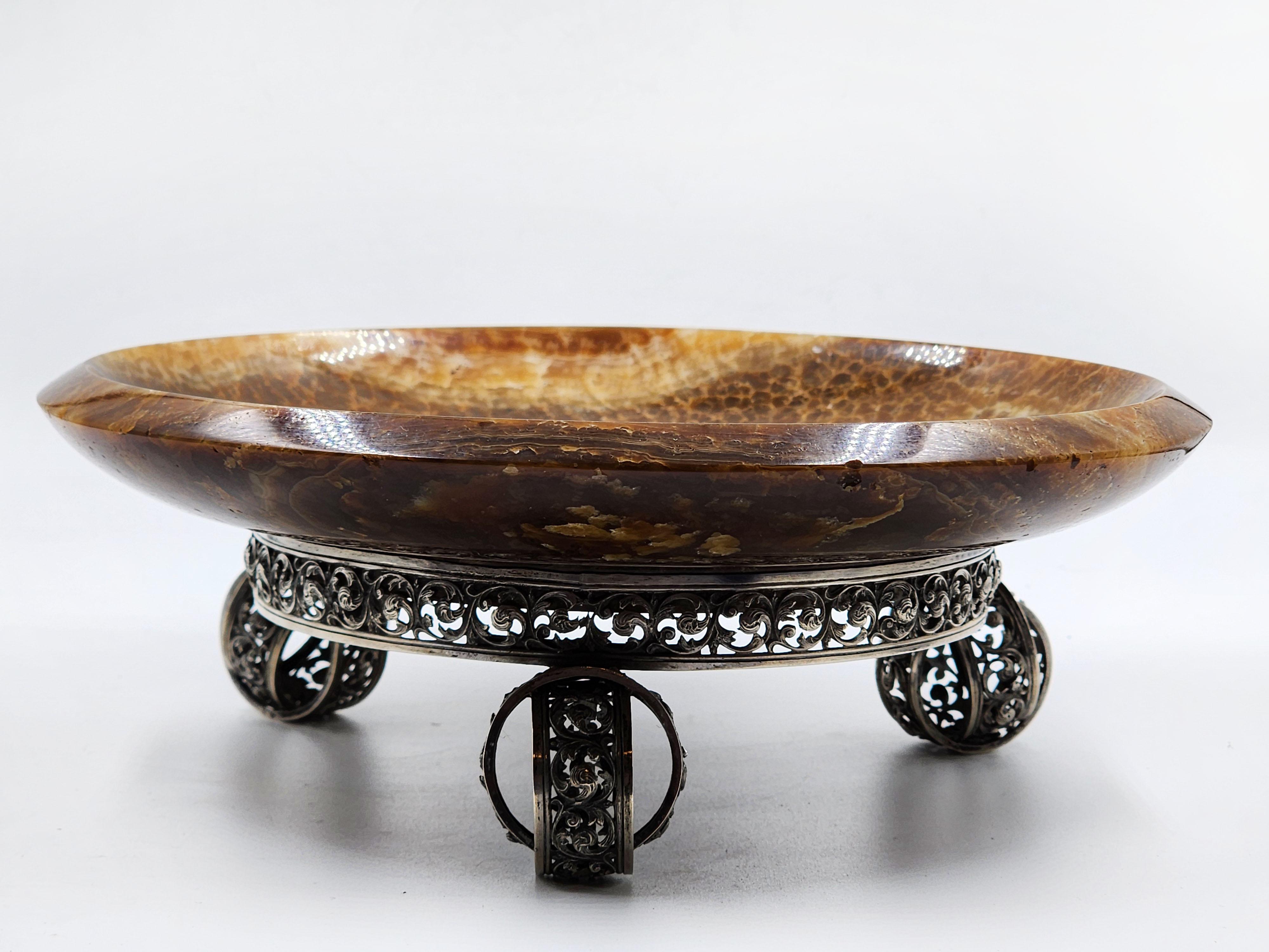 Rara ciotola antica russa in argento con agata
Bellissima ciotola di agata sostenuta da una base con motivi a volute traforate in argento russo; i piedi sono costituiti da due anelli inseriti l'uno nell'altro.
Questa ciotola potrebbe essere un pezzo
