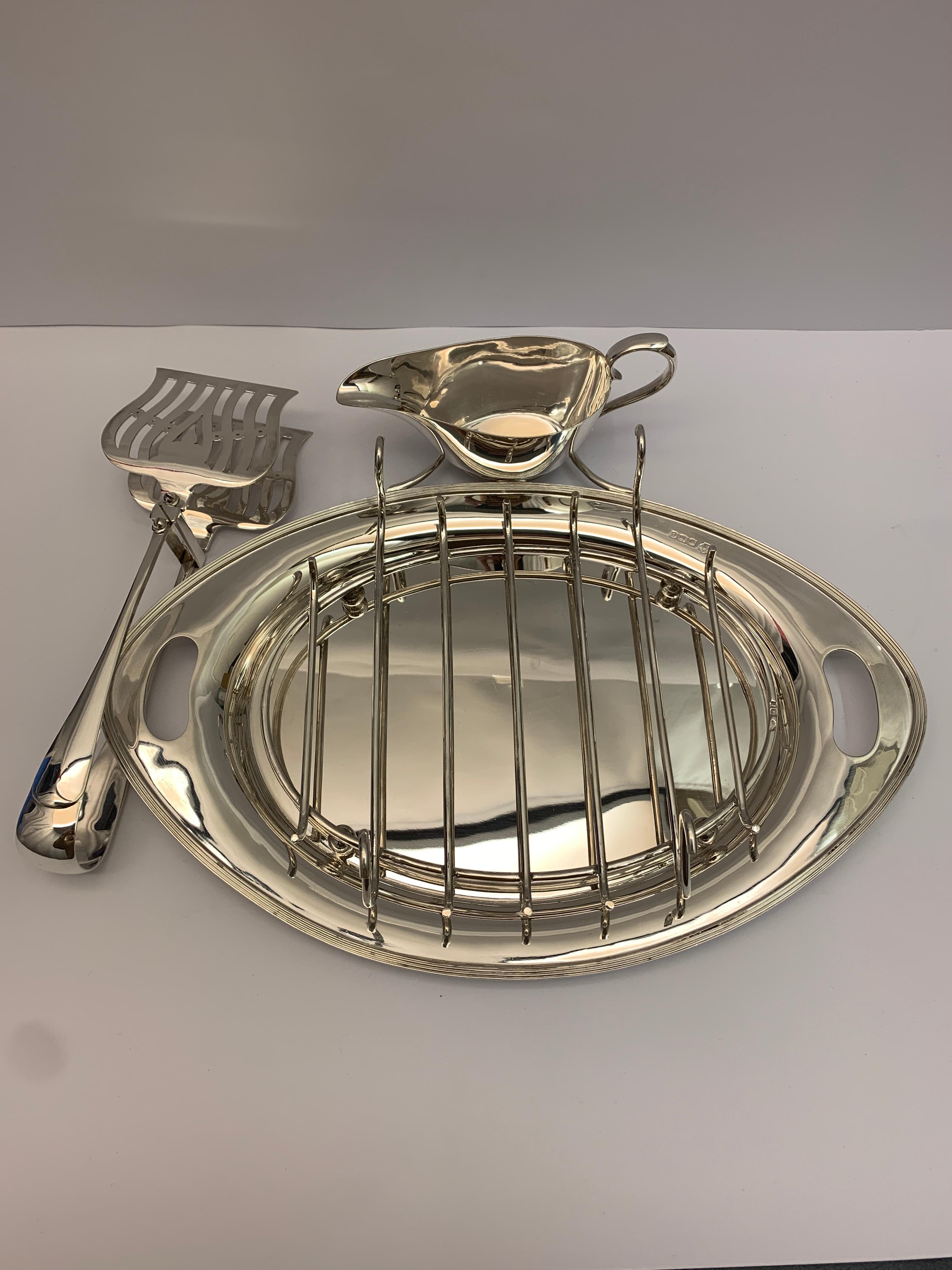 A rare antique silver asparagus serving dish with silver serving tongs, rack and a silver sauce boat.

 