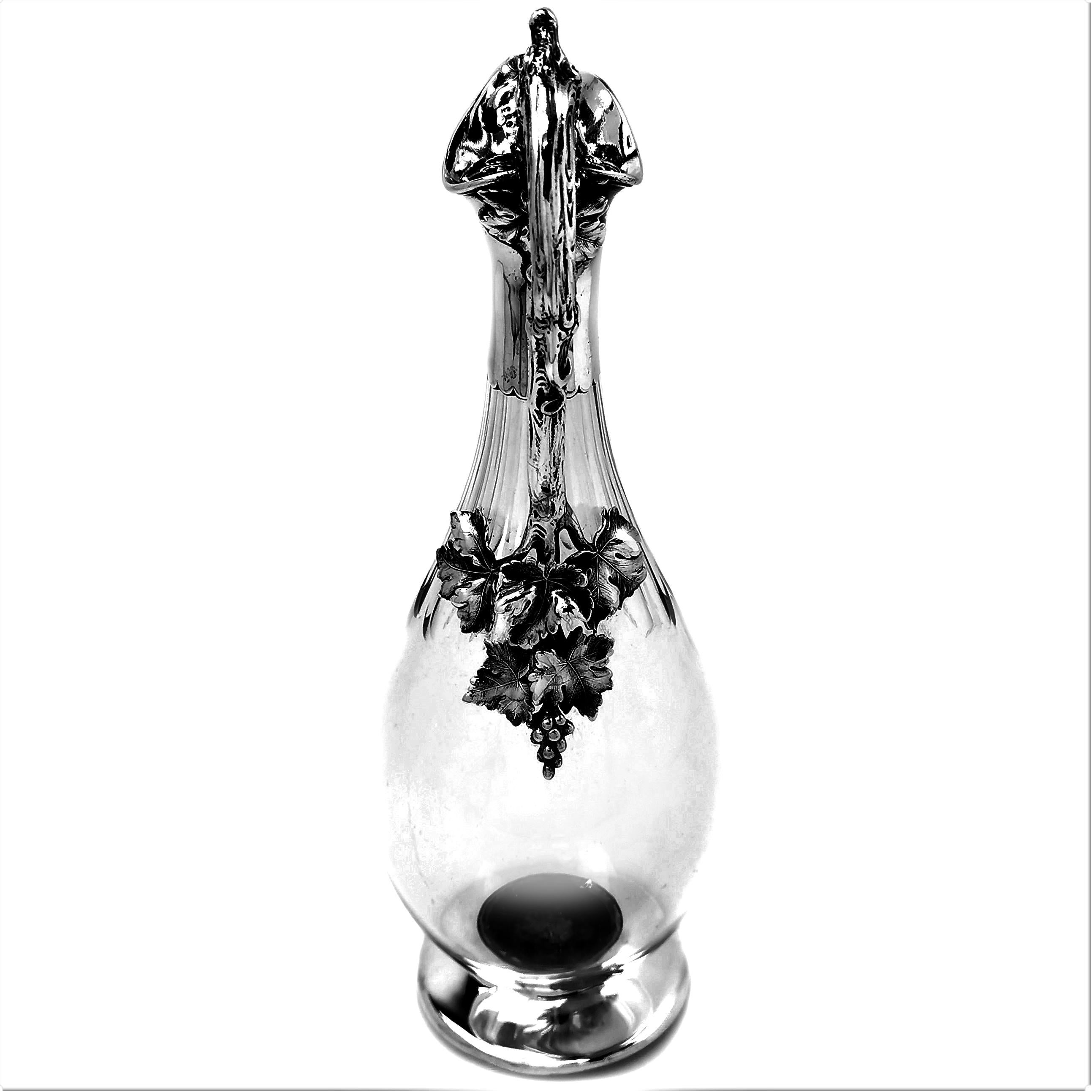 A magnificent Antique Victorian Sterling Silver Mounted Claret Jug with a clear glass body. The Jug boasts an impressive handle created in the shape of a vine branch with leaves and vines applied. The neck of the Jug and spread foot are plain