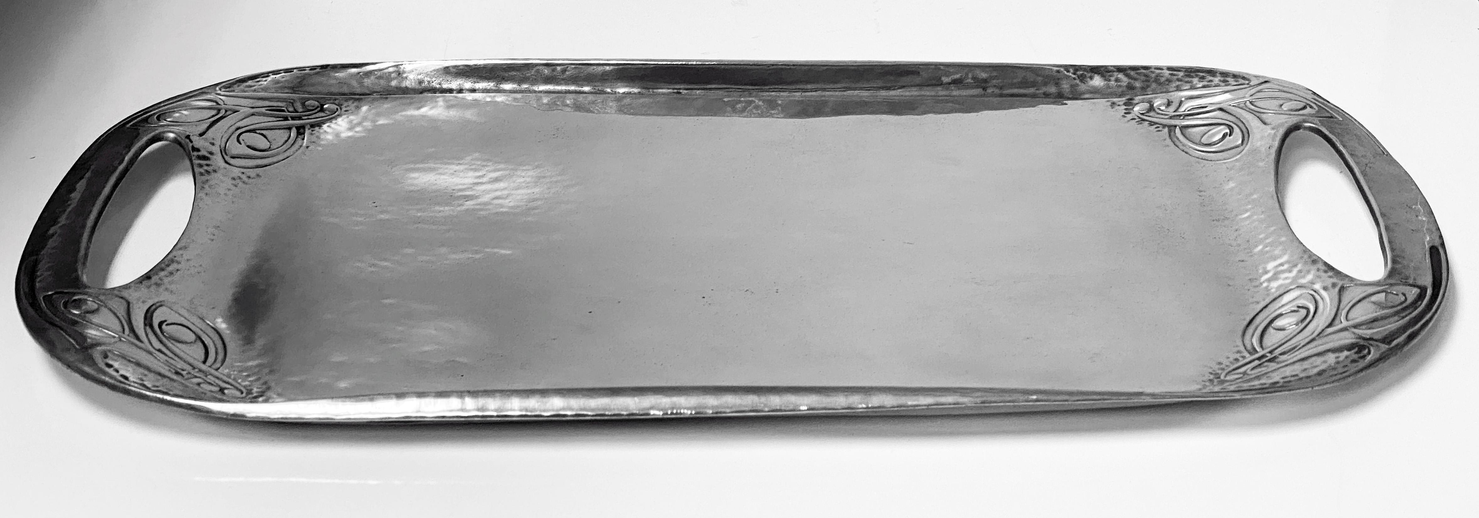 Liberty and Co hammered pewter Tray, designed by Archibald Knox, 1902-1905 design number 0309. Measures: 18.00 x 9.75 inches. The tray centre plain with open kidney handles and cornices of intertwining celtic knot decoration. Liberty Tudric marks