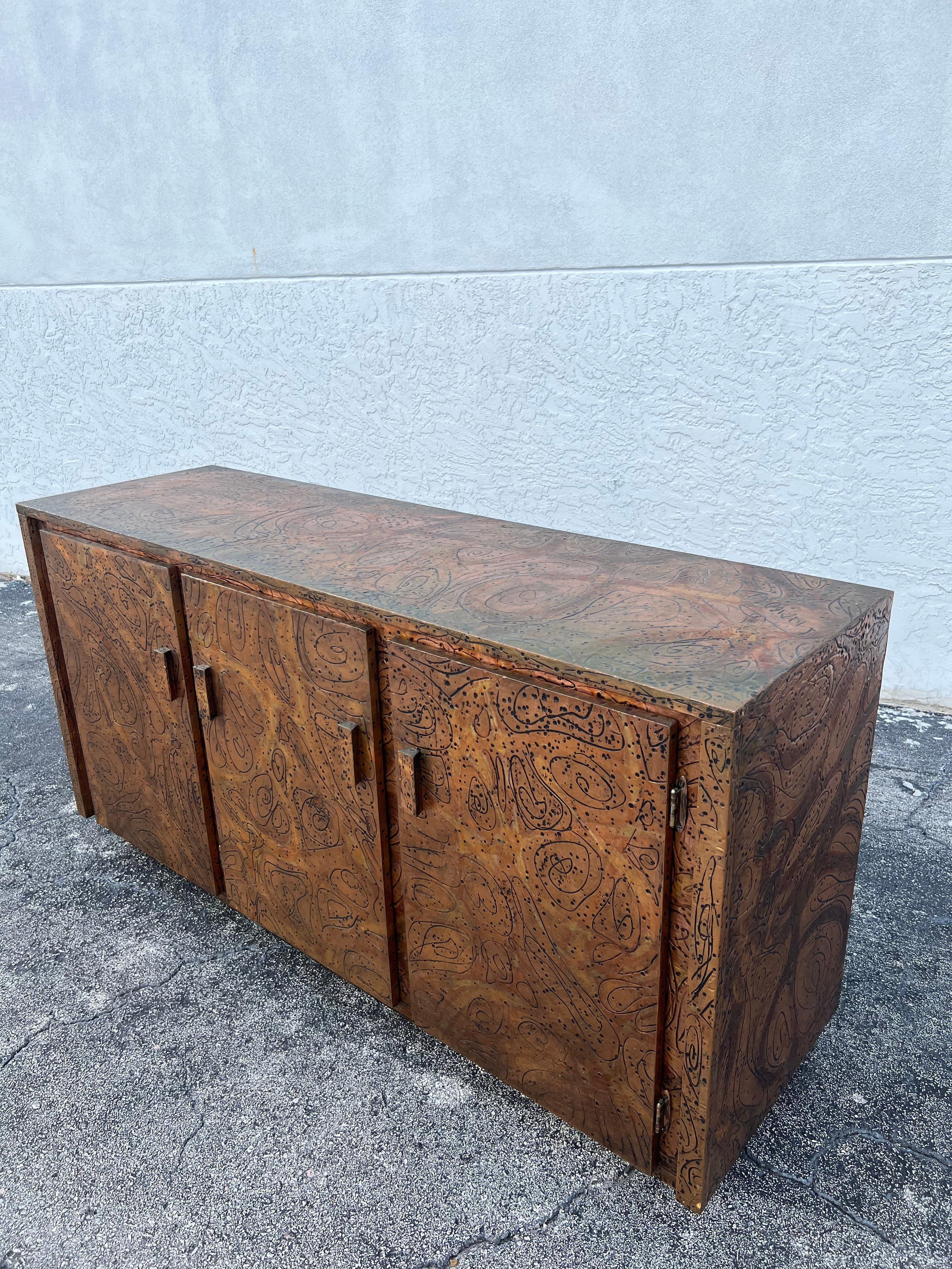Rare Arenson Studios cooper clad credenza. Hand engraved abstract designs throughout. Interior burlap shows signs of wear and minor areas of wear to the clad (please refer to photos). Some looseness on top surface where the copper lifted from the
