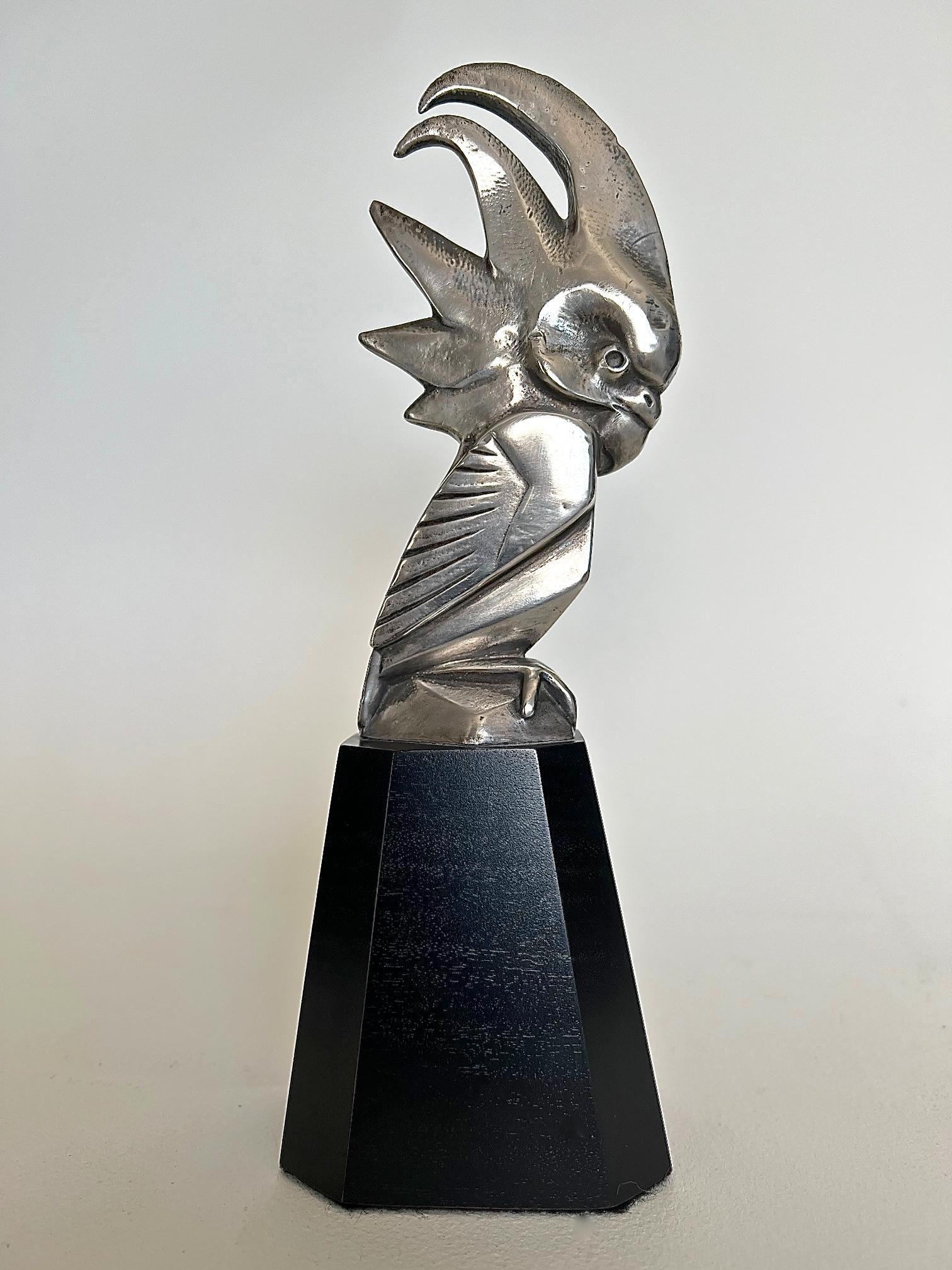 A rare silvered bronze car mascot / hood ornament modeled as a stylised cockatoo. Mounted on a custom made polygonal wooden base. Signed in the bronze 