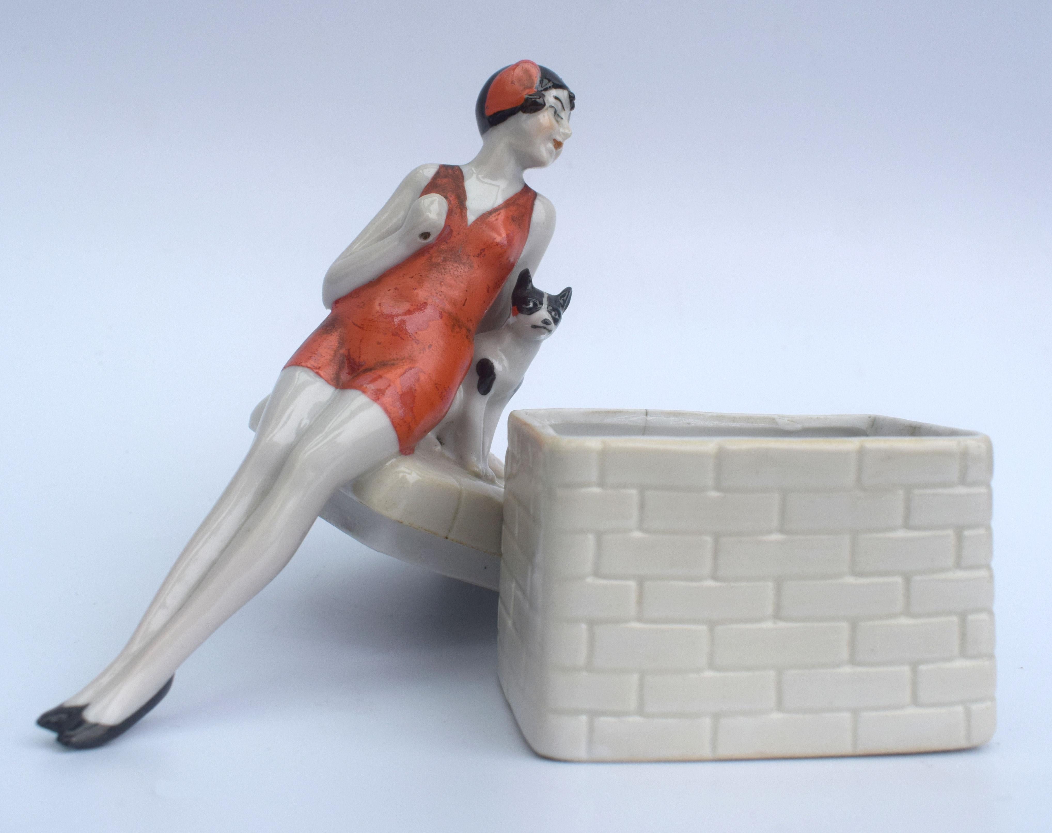 Dating to the 1930s this very attractive and rare Art Deco trinket powder jar or box which is part of the half doll family. Depicts a flapper girl leaning on a brick box with her dog, marked numbers to the base are 5660. The attention to detail is