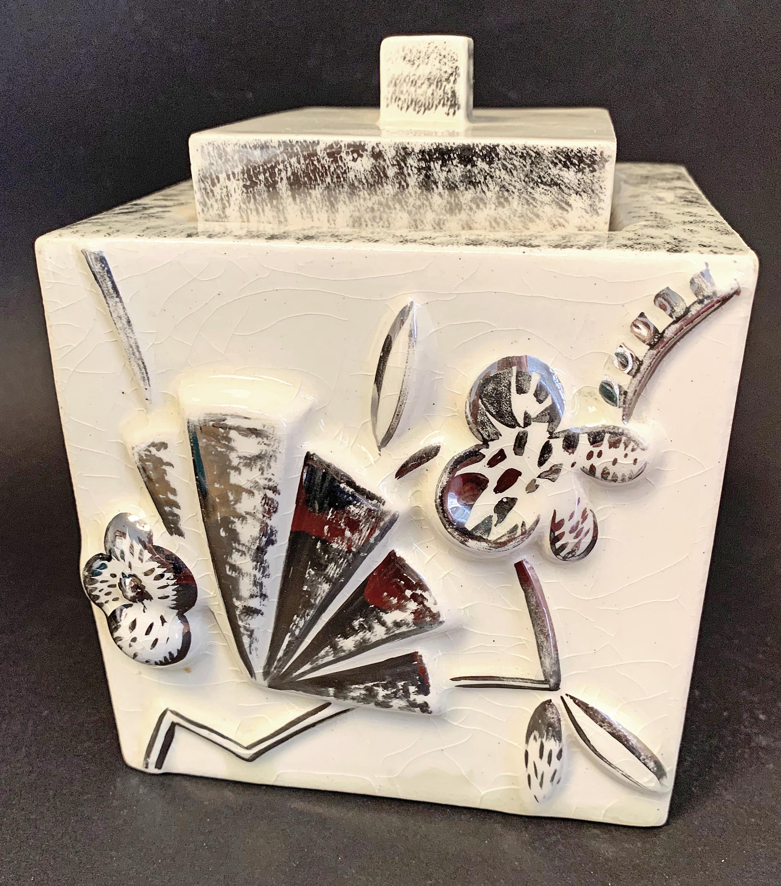 Striking in its originality and abstraction, this high-style Art Deco lidded porcelain box is decorated with a series of foliate and abstract motifs, executed in silver glaze, that hint at gears and fans. The combination of a pale ivory glaze