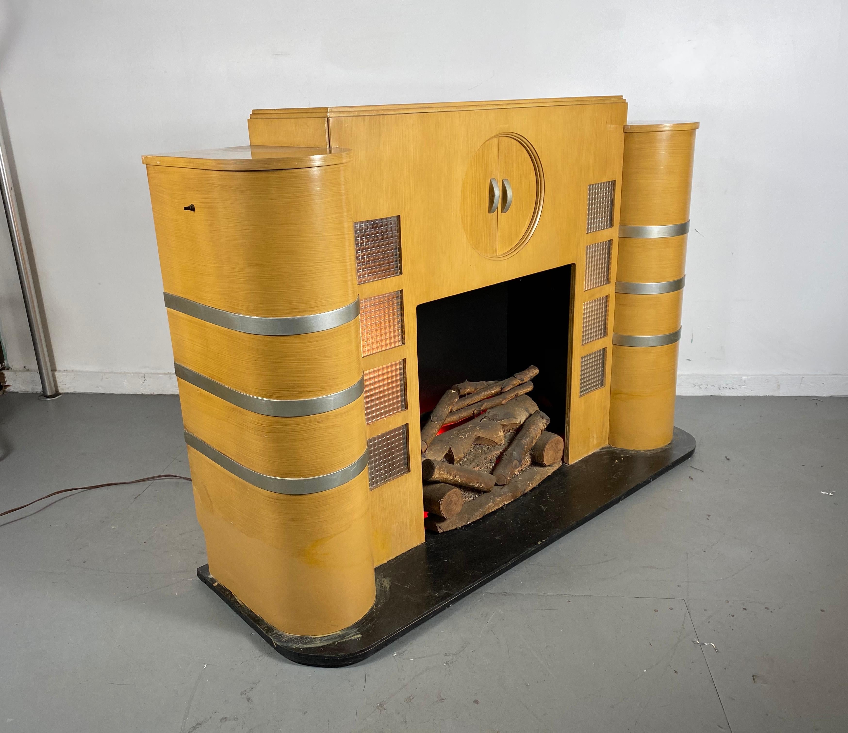Art Deco, modern streamlined free standing mantel, beautiful bent plywood, Classic Deco speed lines, ribbed block glass detailing, backlit, center circle opens, two sliding doors, retains original fake logs, (lite with red bulbs) hand delivery avail