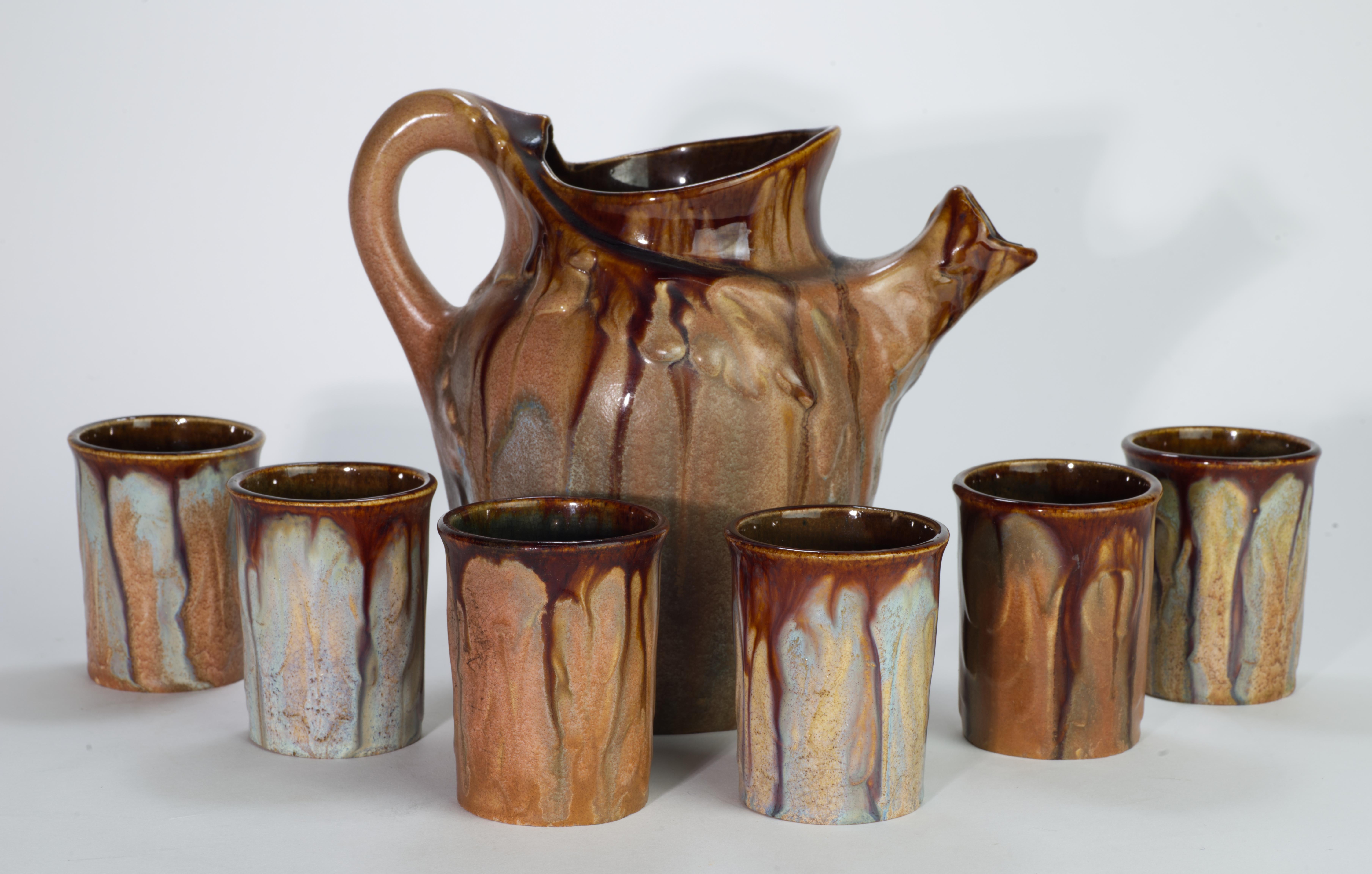  Rare set of a pitcher and 6 glasses or cups was created in characteristic Belgian Art Nouveau style with the use of warm, earthy tones and varied glaze finish on lightly textured shapes of the pieces. Predominantly brown-beige palette is