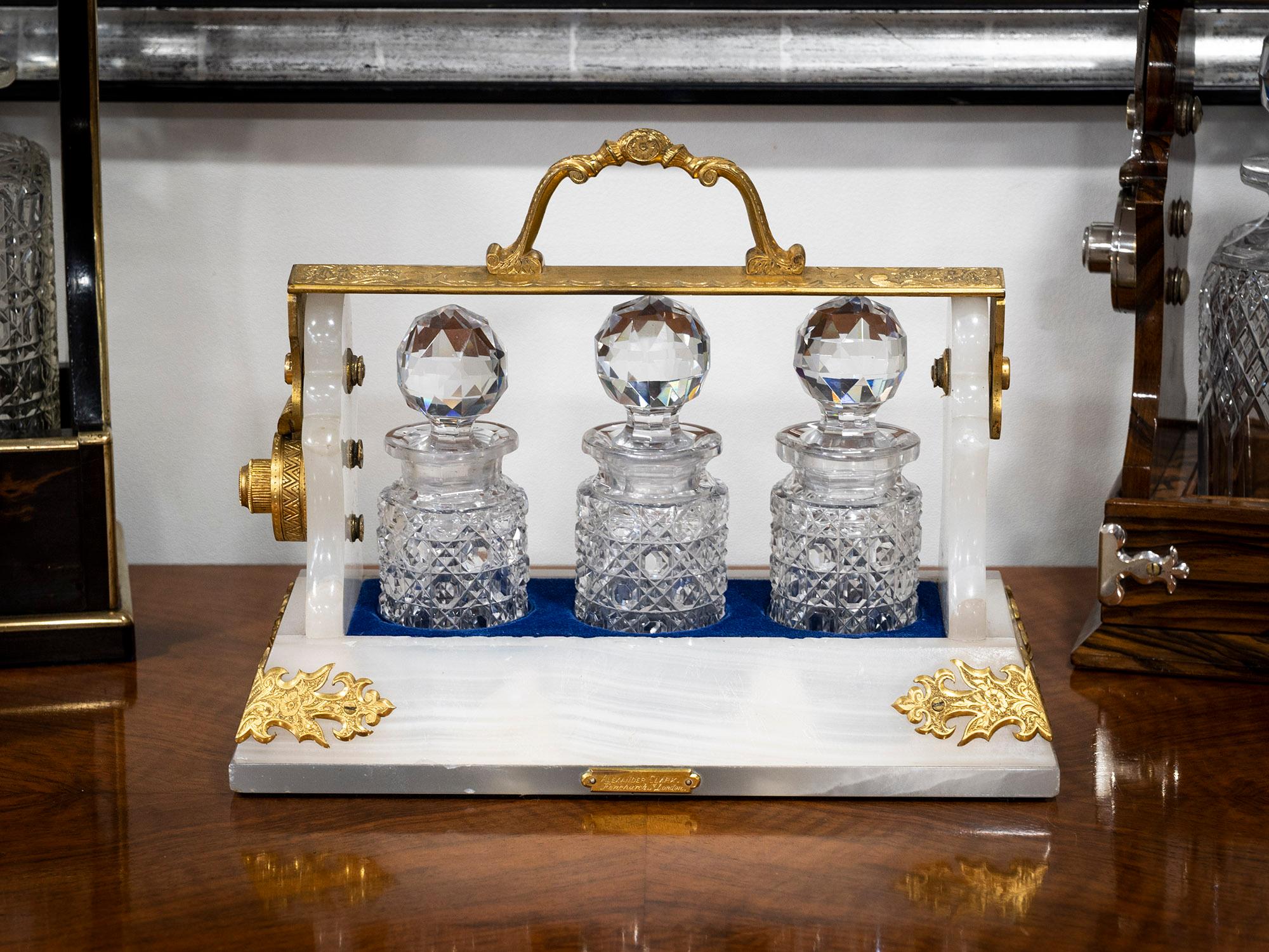 The Tantalus is of typical form however it is of rare miniature size measuring only 22cm high x 26cm wide. The Tantalus is made from white onyx with scrolling ormolu mounts and an ormolu hinged carry handle. The carry handle is beautifully engraved