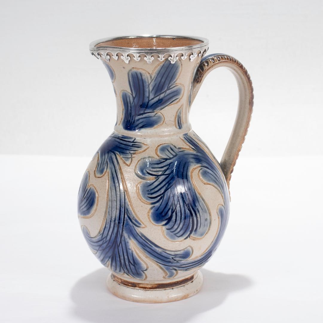 A rare English silver mounted stoneware pitcher by Arthur Boulton Barlow for Doulton Lambeth.

The diminutive pitcher has incised leafwork throughout that is decorated in blue slip. Borders and highlights are decorated in brown slip. 

The sterling