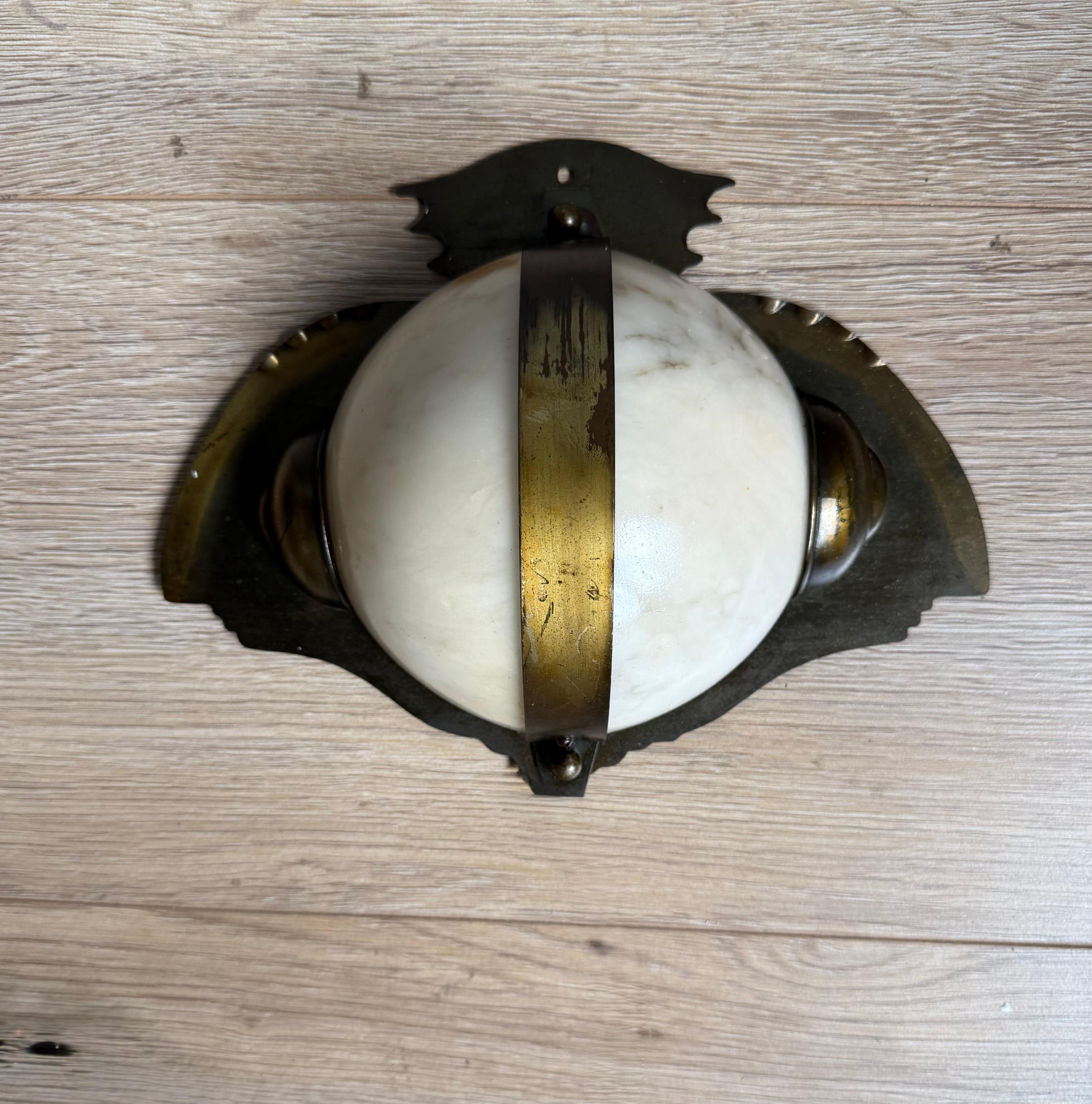 Antique Art Deco brass & alabaster wall light with owl-like silhouette black-plate.

The sculptural design features a domed alabaster shade encircled by a gilt brass band, mounted on a decorative brass backplate. Its stylized silhouette evokes the