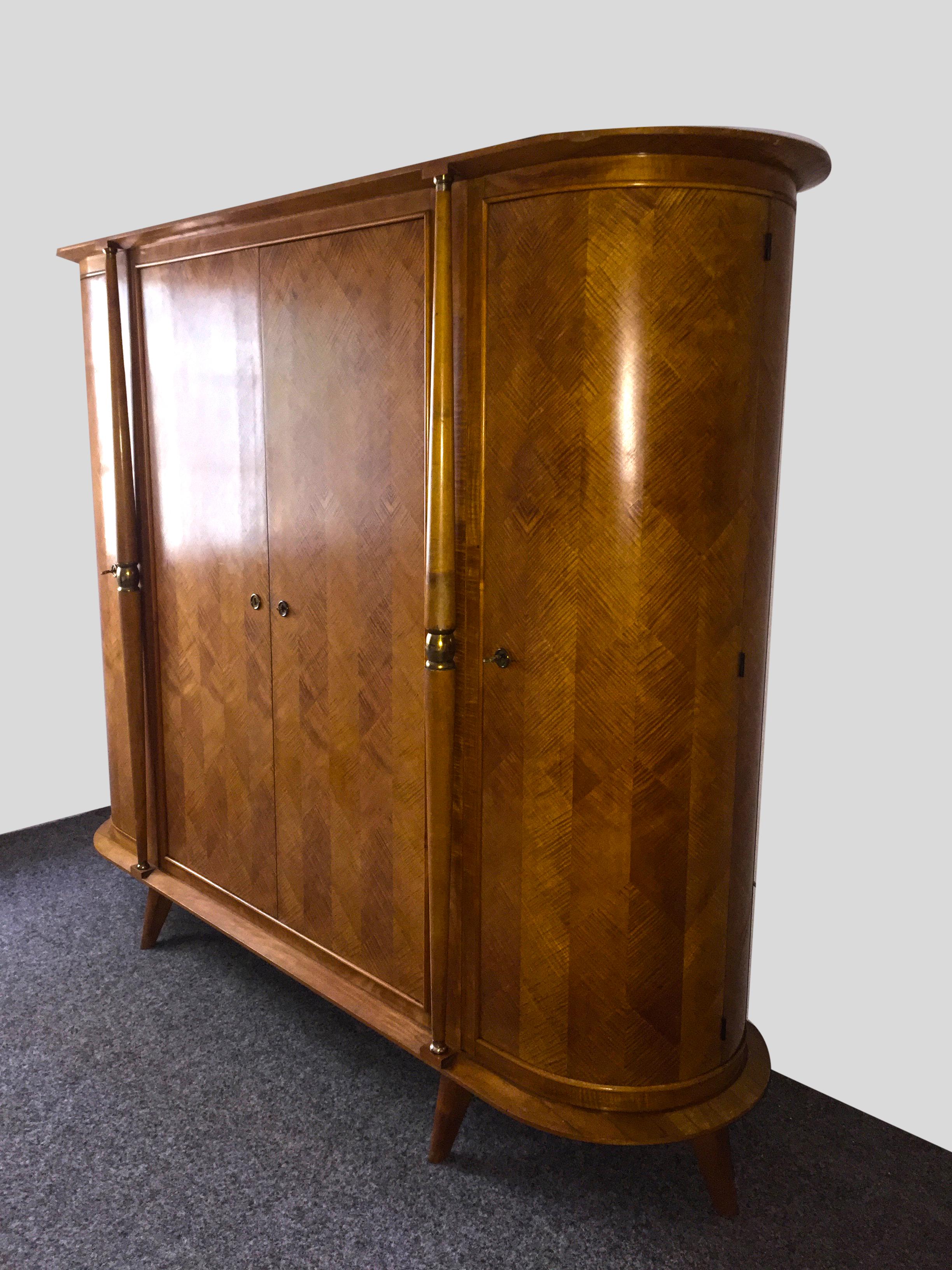 Exceptional as design and in the style of Andre Arbus, French, Art Deco oval armoire of sycamore. Four doors, three compartments, the two outer ones with shelves, the interior is empty. Mirror on one of the inner doors. Two decorative columns with