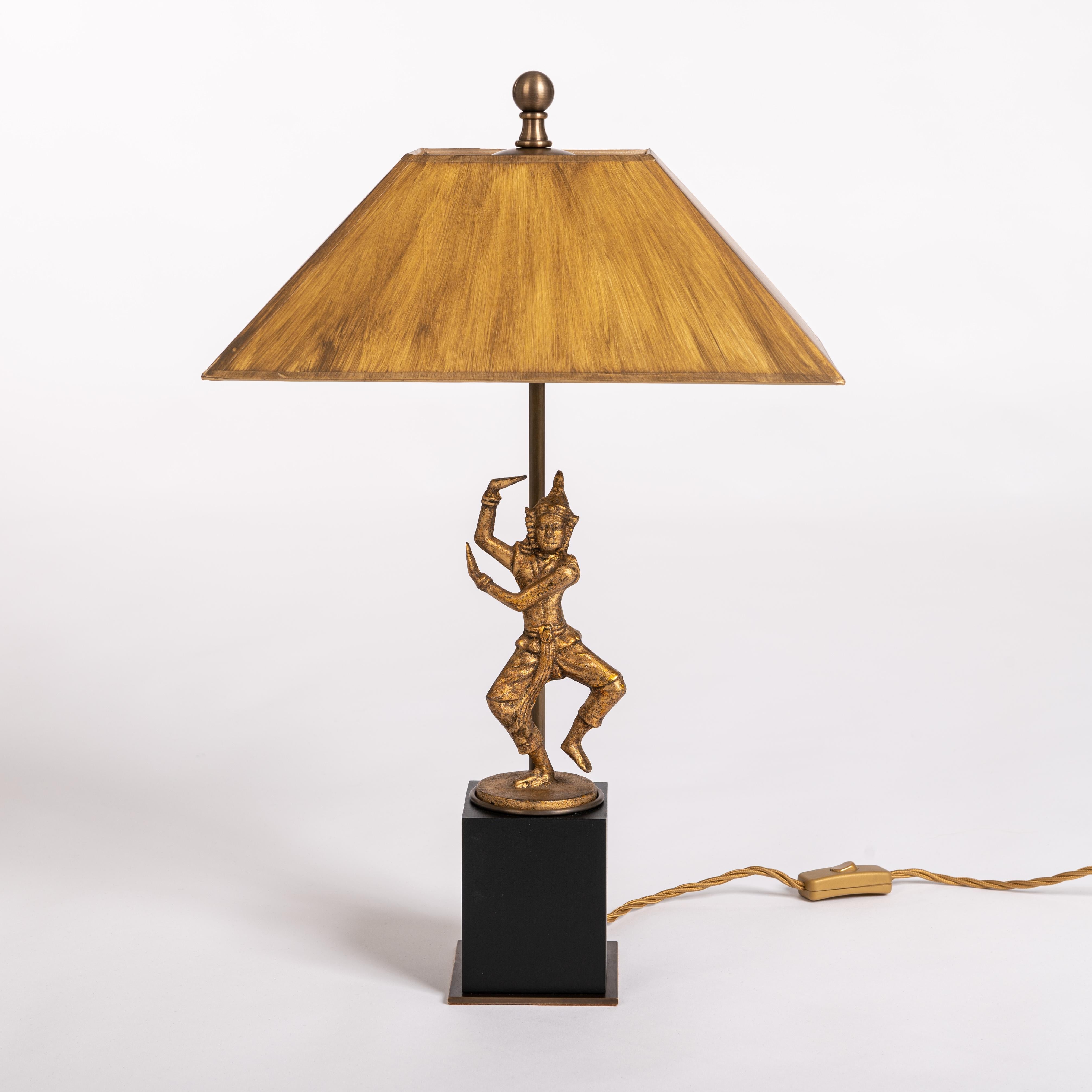 A table lamp like a piece of jewelry an eye-catcher.
A small, moving Buddhist dancer-sculpture became the focus of a table lamp.
The object from Myanmar is in its original condition and stands on a wooden base. 
The purpose built lamp construction