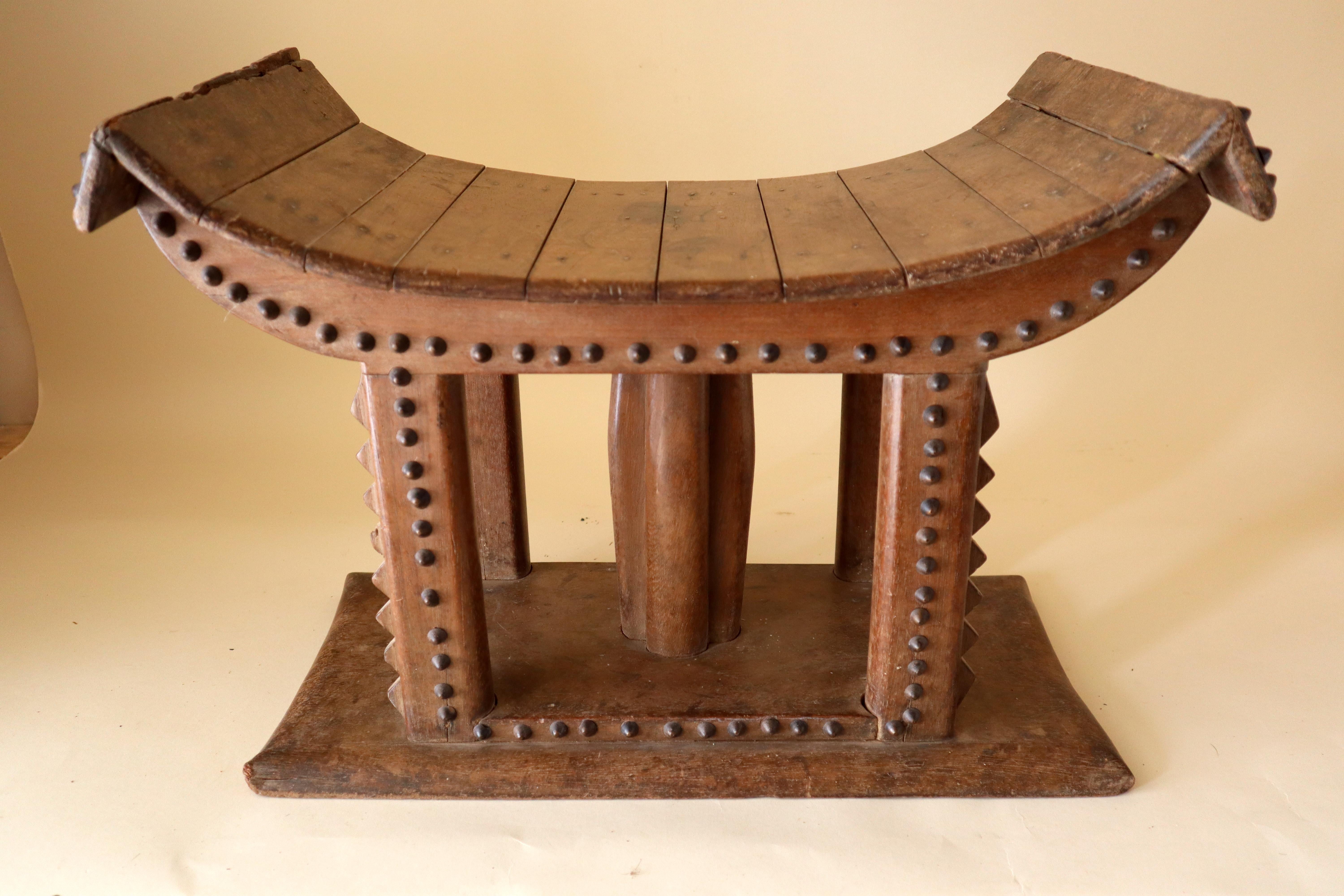 A rare type of Akan stool or seat. Rare because it is assembled instead of being carved out of one large piece of wood and is trimmed on most edges with bead-like rows of decorative brass upholstery tacks. The Ashanti, Fante, and Baule are subgroups