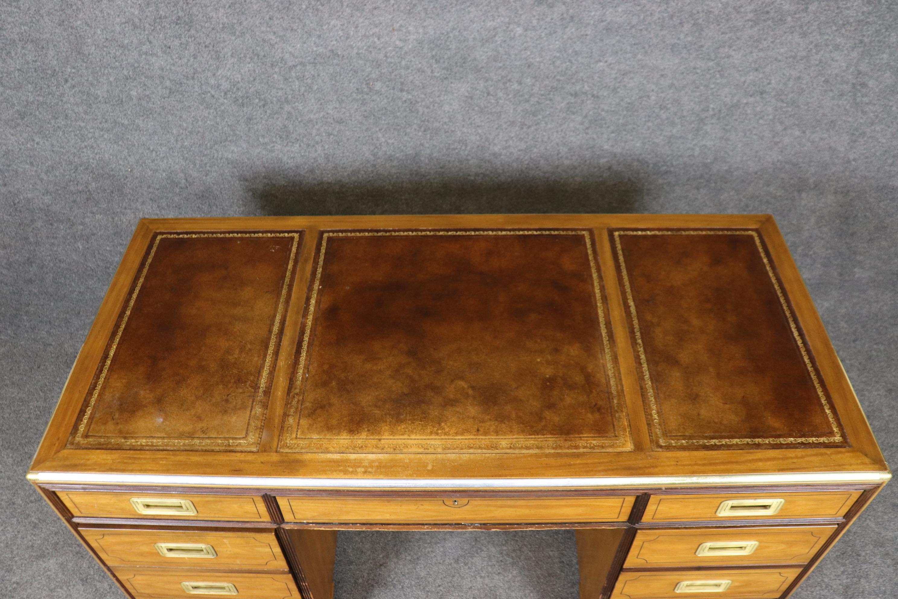 This is a rare find indeed. This gorgeous 1970s era Baker Furniture company campaign style desk features a gorgeous hand-tooled gold embossed leather top with fantastic patina and aged brown leather. The desk is a mahogany case with satnwood veneer