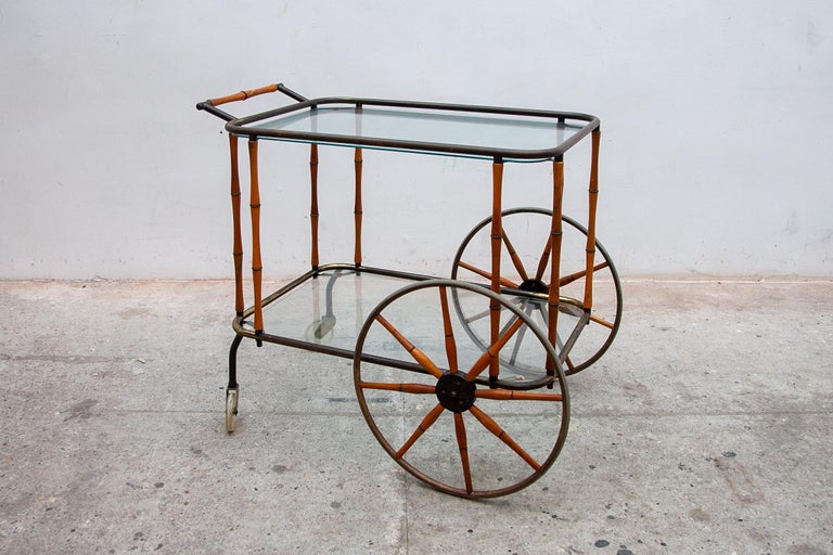 Beautiful rare brass and bamboo wood Hollywood regency drinks trolley, bar cart with two glass shelves. Brass frame with bamboo handle, sides and decorative oversized wheels. In original vintage condition with the darkened patina. Wonderfull design