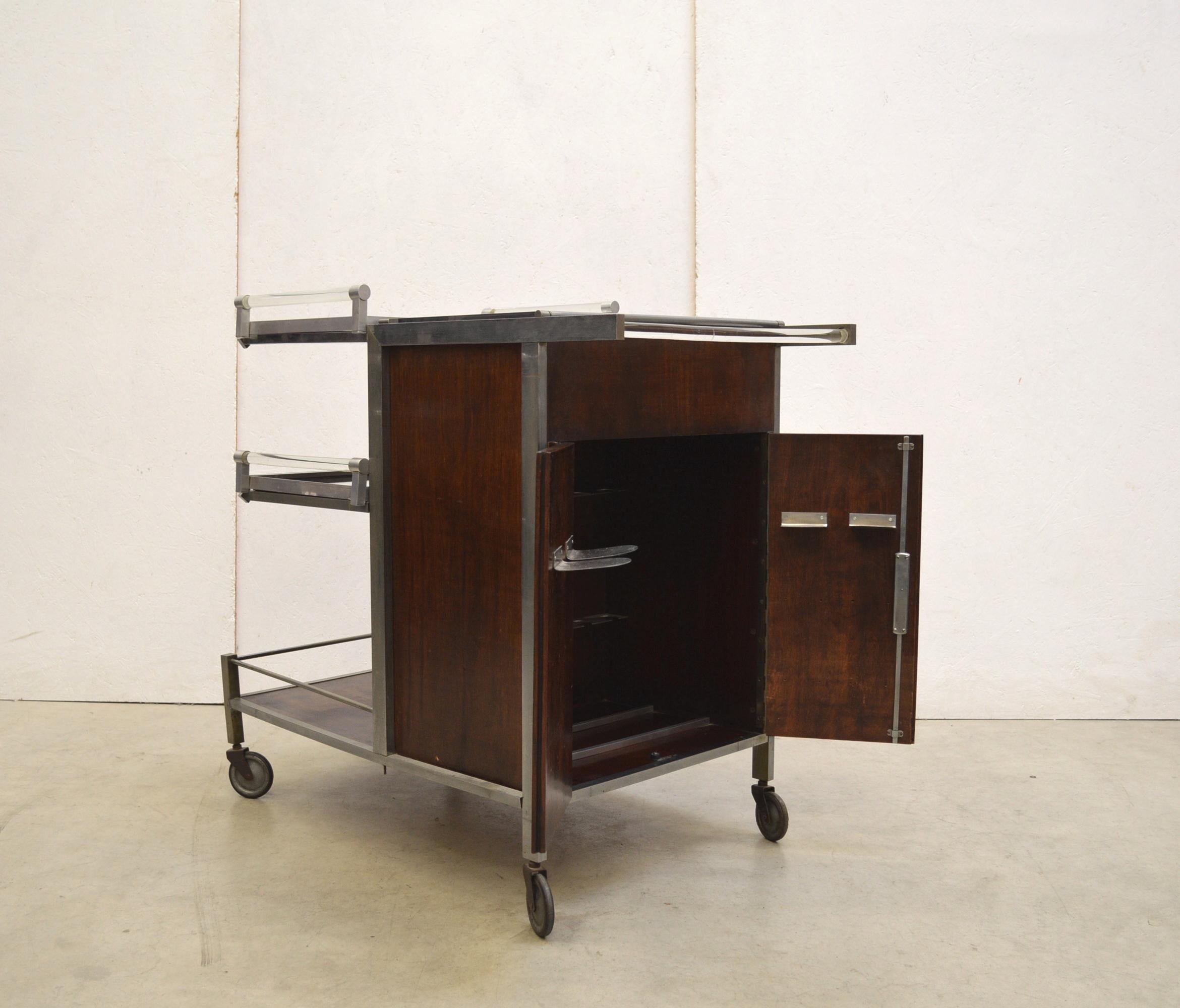A wonderful bar cart trolley by Jacques Adnet ( France 1900 - 1984) made in the 1930s.
The bar card features chromed metal parts, aluminium and mahogany veneer structure.

Wonderful bar with 2 doors. Mirrored glass trays which are moveable.
Also