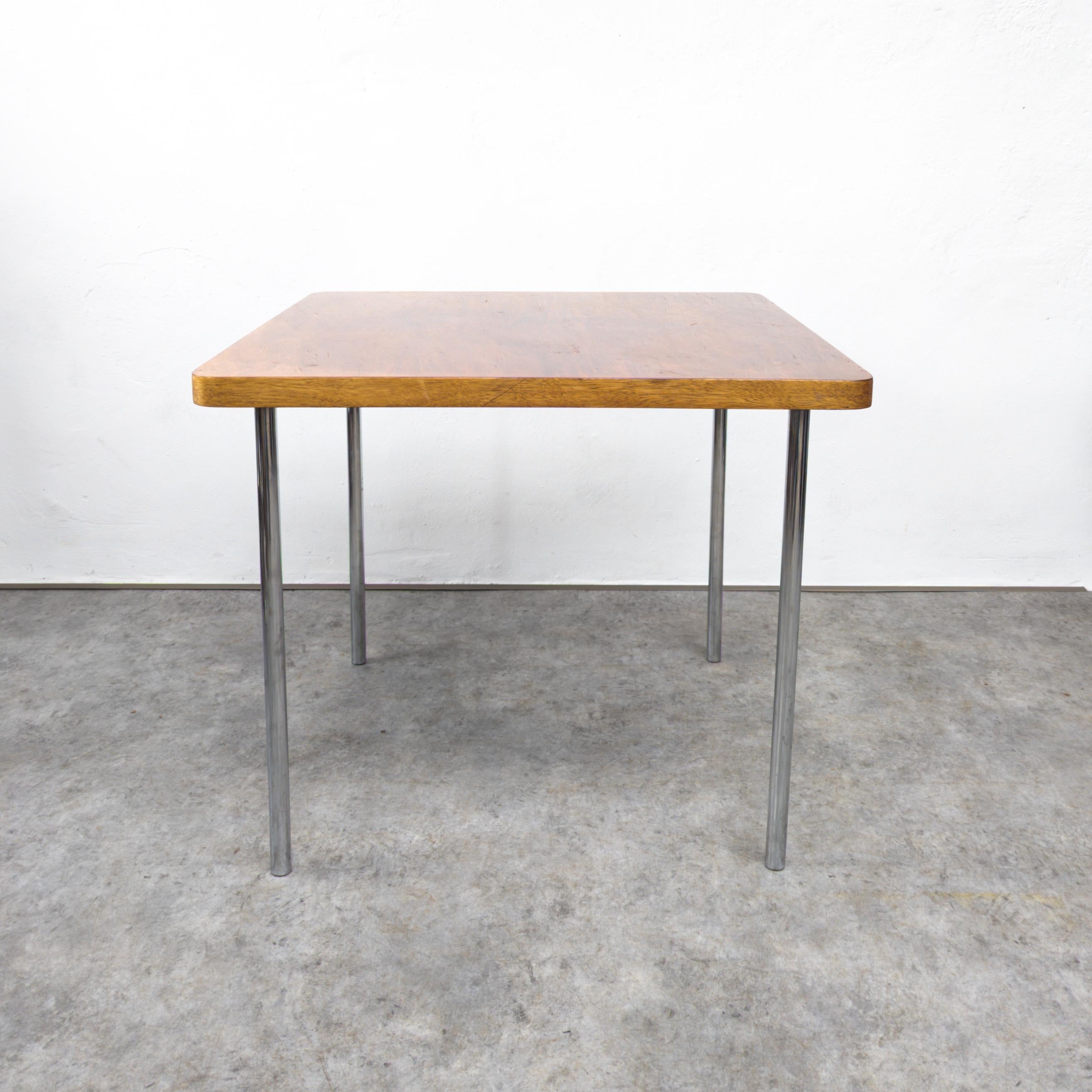The Thonet B 14 table, designed by Marcel Breuer, is a classic piece of furniture known for its innovative use of tubular steel and geometric forms. It features a square wooden top supported by straight chrome plated steel legs, creating a simple
