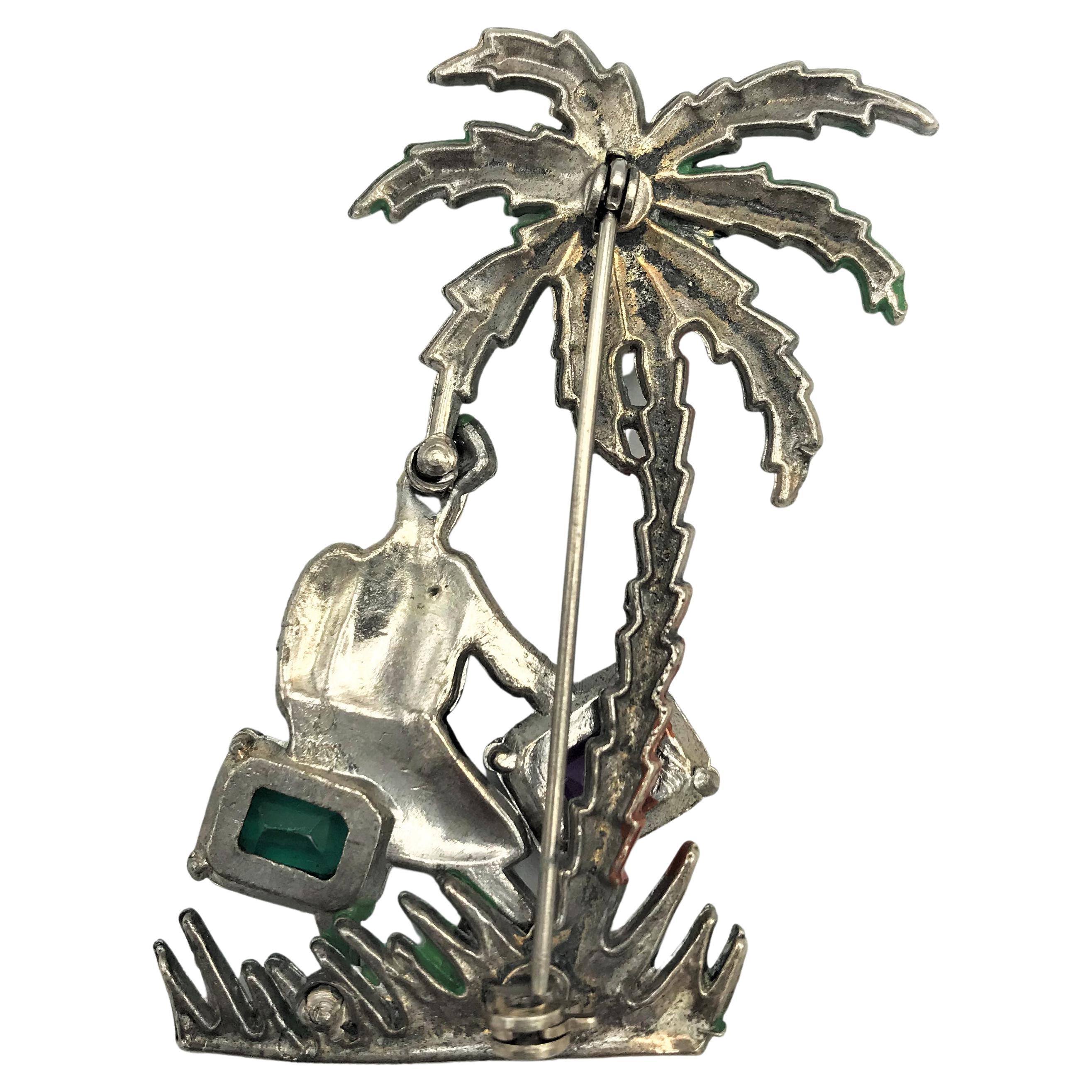 Superb Baumann Massa suitcase lady under a spreading palm tree brooch.
The suitcase is set with faceted rhinestones( they are the suitcase), one pink and one green.
She is stepping through the enameled grass under a large palm tree.
She is in great