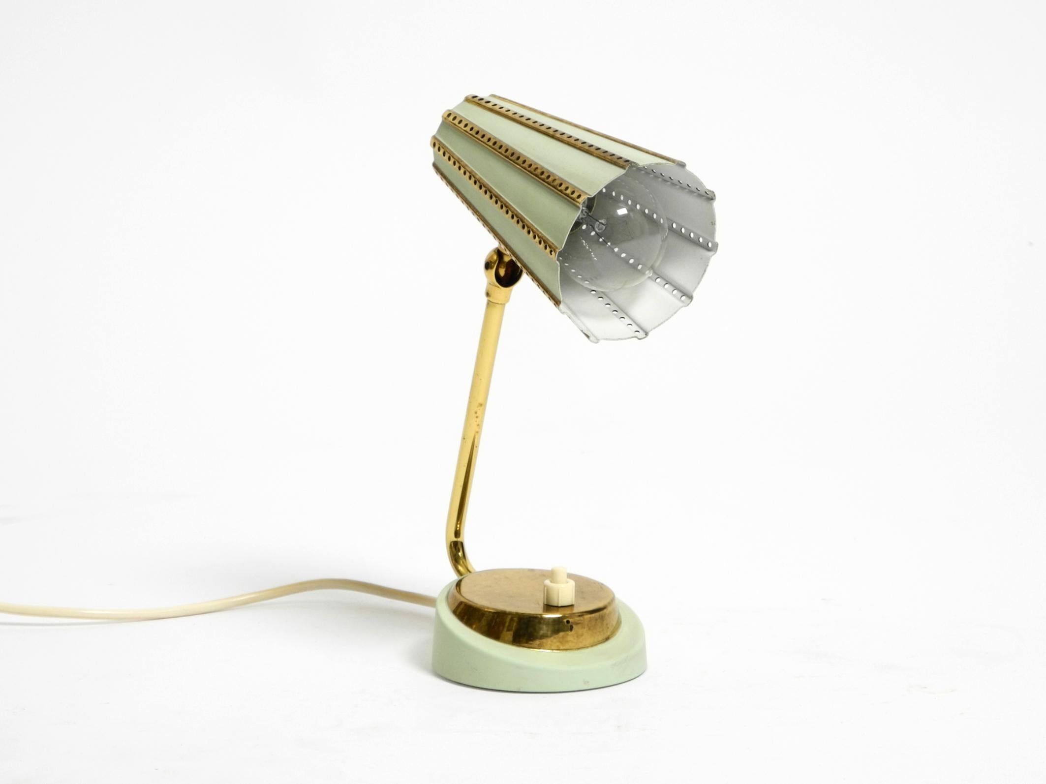 Rare, very beautiful mid-century brass night table lamp with a perforated metal shade.
Very beautiful 1950s design with a great patina. The shade is steplessly adjustable up and down. The entire lamp is made of brass, partially painted in mint