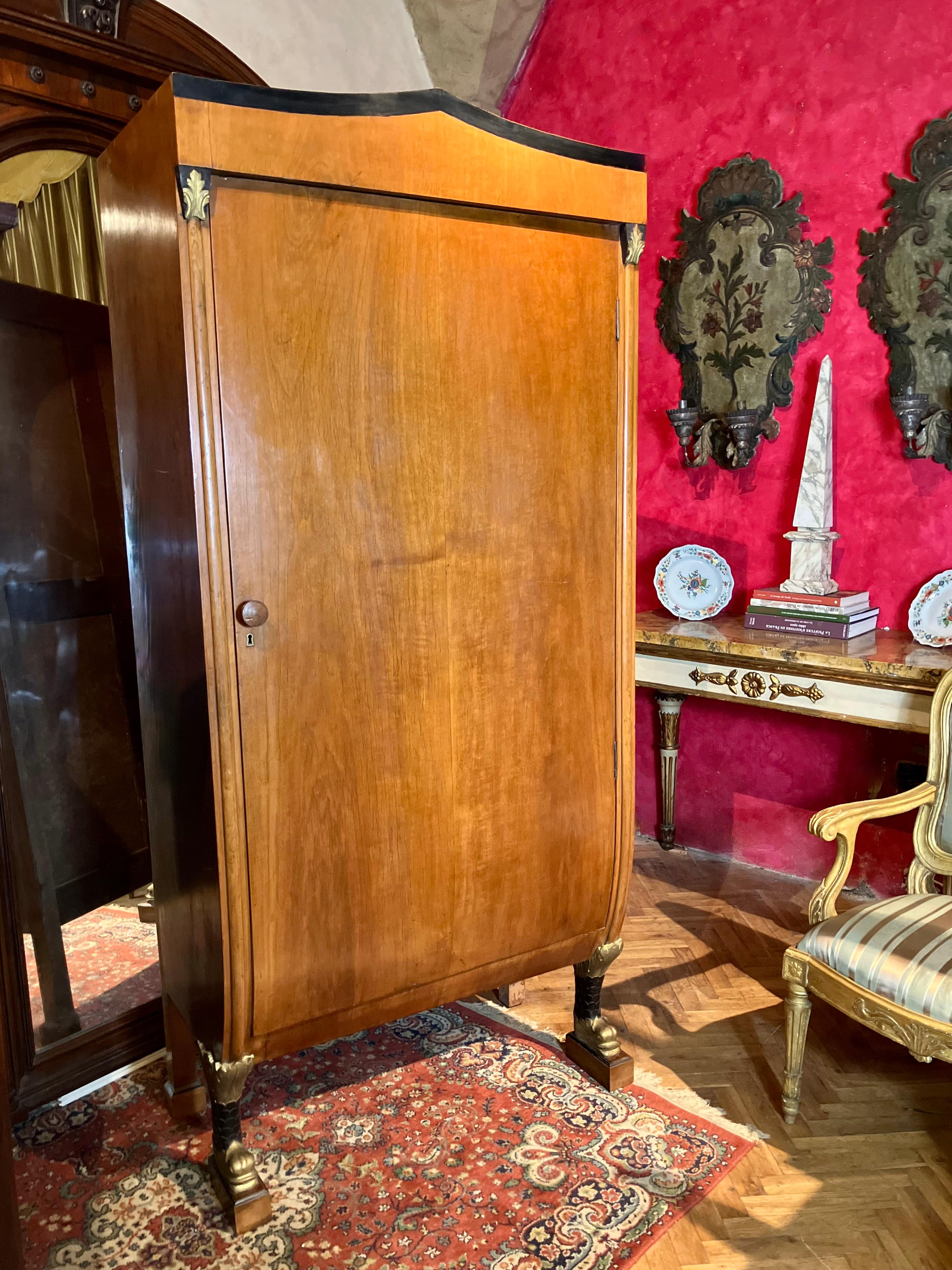 Ein wirklich außergewöhnlicher eintüriger Biedermeier-Schrank aus honigfarbenem Kirschbaumholz. Dieses einzigartige Stück zeichnet sich durch schwarz lackierte und vergoldete Holzdetails, komplizierte Schnitzereien und anmutig geformte Delphinfüße