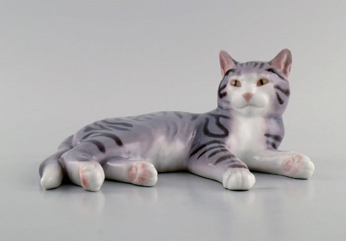 Seltene Porzellanfigur von Bing & Grøndahl. Liegende Katze. 
Modellnummer 2236. 
Anfang des 20. Jahrhunderts.
Maße: 18 x 9,5 cm.
In ausgezeichnetem Zustand.
Gestempelt.
2. Fabrikqualität.