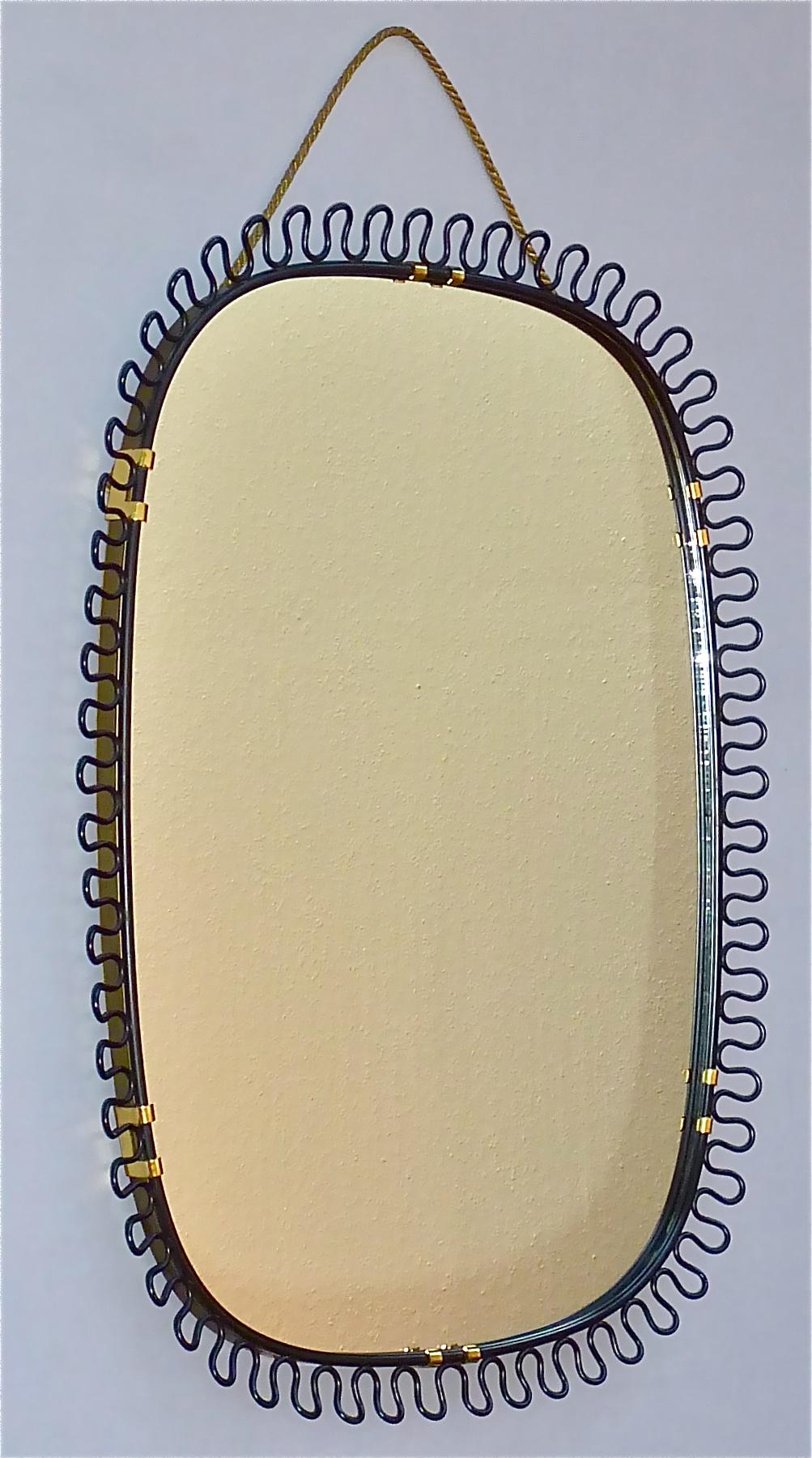 Sculptural and elegant midcentury wall mirror by Josef Frank Austria or Sweden for Svenskt Tenn, circa 1950s which is made of patinated brass metal, a beautiful black enameled loop-wire-decoration, original mirror glass, wood on reverse and with its