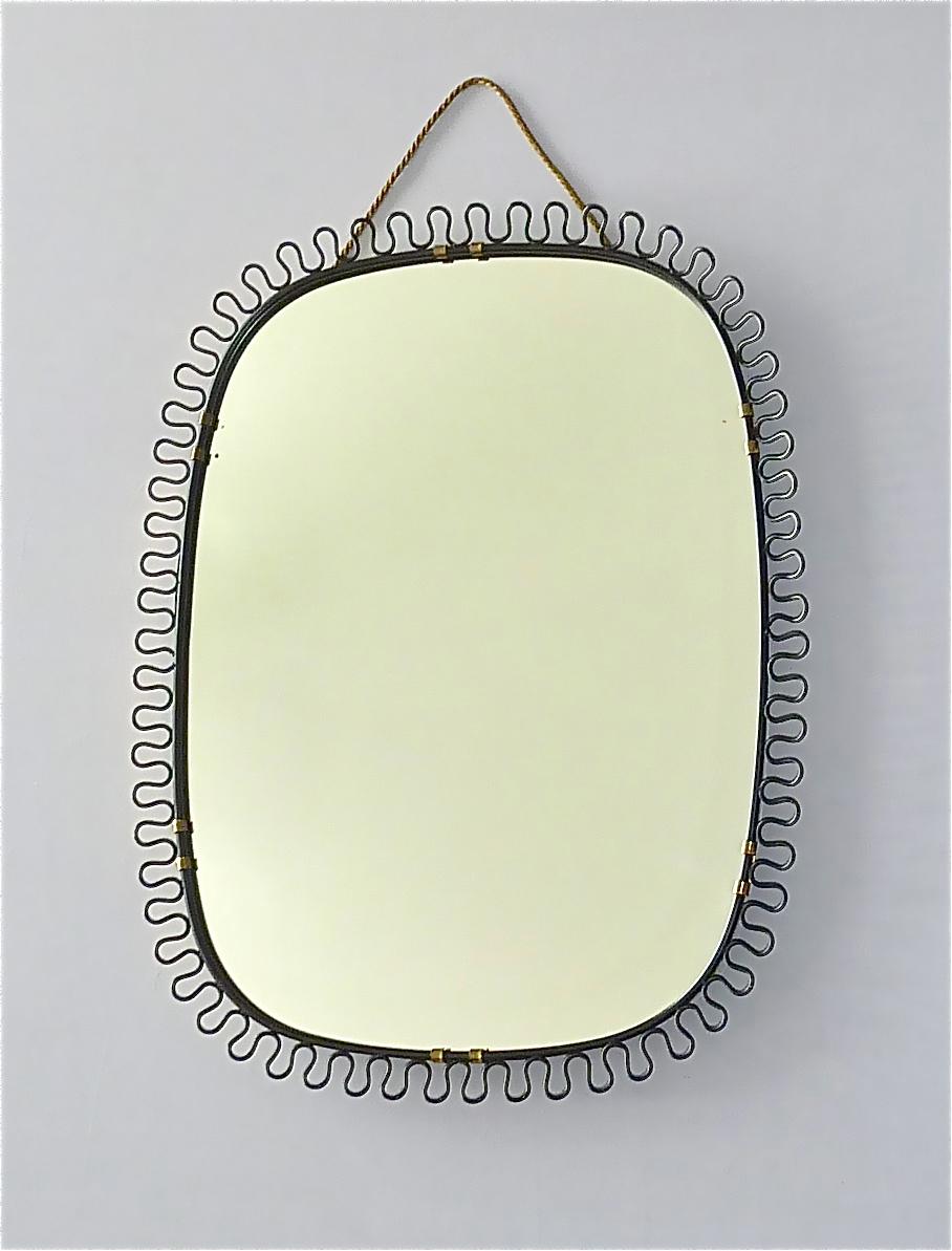 Sculptural and elegant midcentury wall mirror by Josef Frank Austria or Sweden for Svenskt Tenn, circa 1950s which is made of patinated brass metal, a beautiful black enameled loop-wire-decoration, original mirror glass and wood on reverse. The