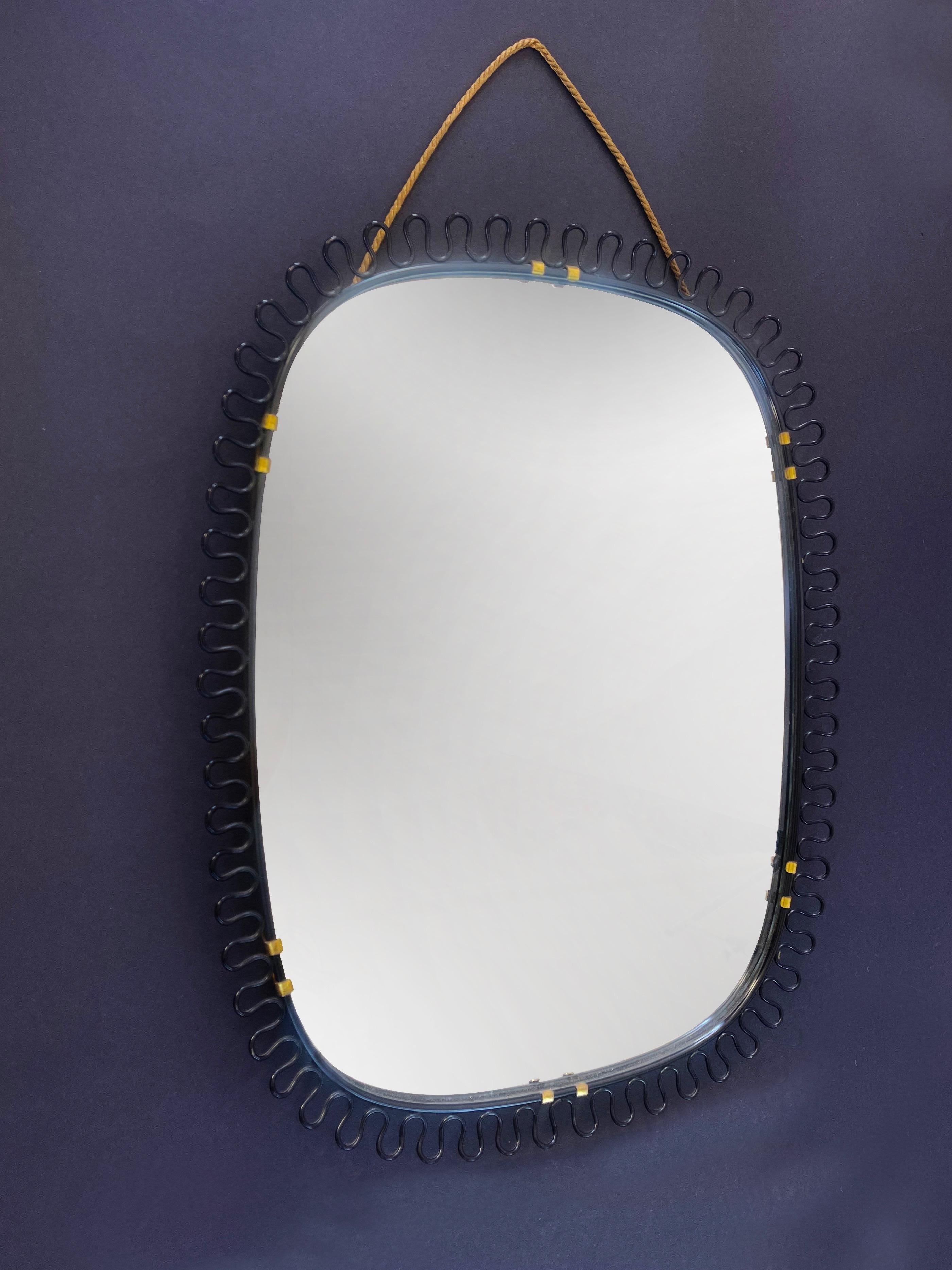 Specchio da parete ovale di stile Mid-Century Modern, scultoreo ed elegante di Josef Frank 
Austria/Svezia per Svenskt Tenn, anni '50 circa. 
Realizzato in metallo nero con una bella decorazione a filo, dettagli in ottone dorato e scintillante,