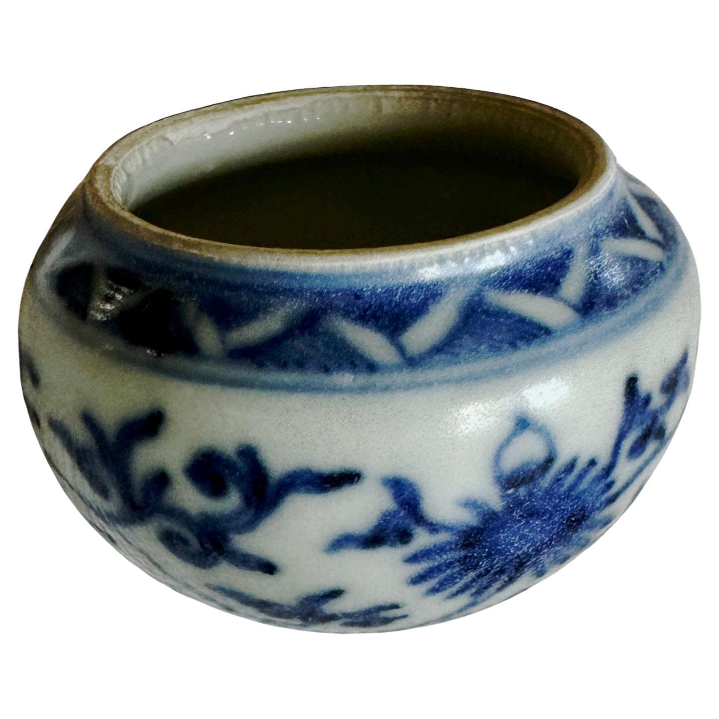 A small blue and white bird-feeder of circular form with short neck, one side set with two small loup handles, the base slightly pointed, painted with lotus heads growing from scrolling stems with curled leaves between a double-line border