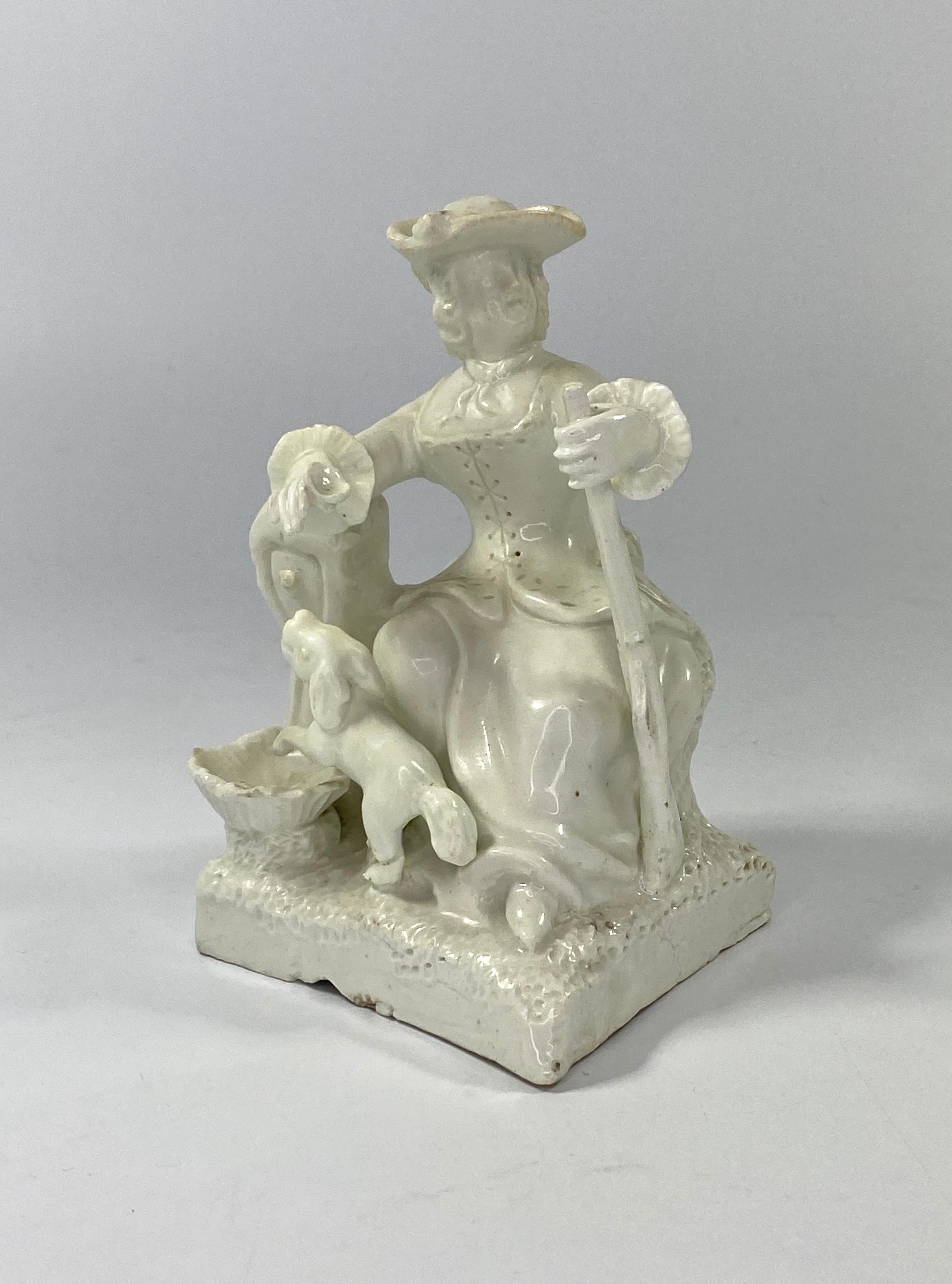 A rare bow porcelain figure of a Huntress, c. 1750. The white glazed figure of a seated lady, holding a gun in her left hand. She holds a glass in her right hand, whilst resting her arm on a fountain, above a shell reservoir. A dog, standing on its