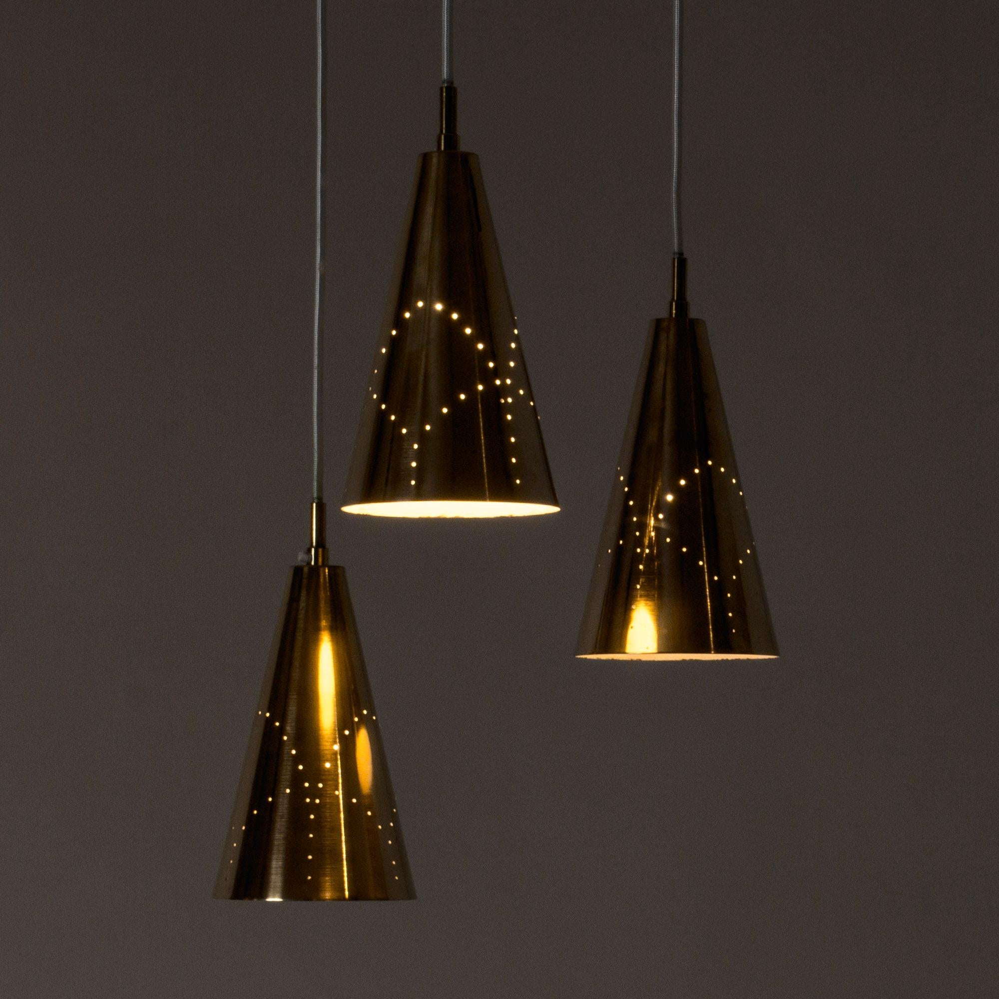 Rara lampada da soffitto di Hans-Agne Jakobsson. I tre paralumi in ottone sono traforati con un motivo che risulta particolarmente bello quando sono illuminati. I cordoni tessili sono uniti da un braccio in ottone diviso in tre parti con una palla
