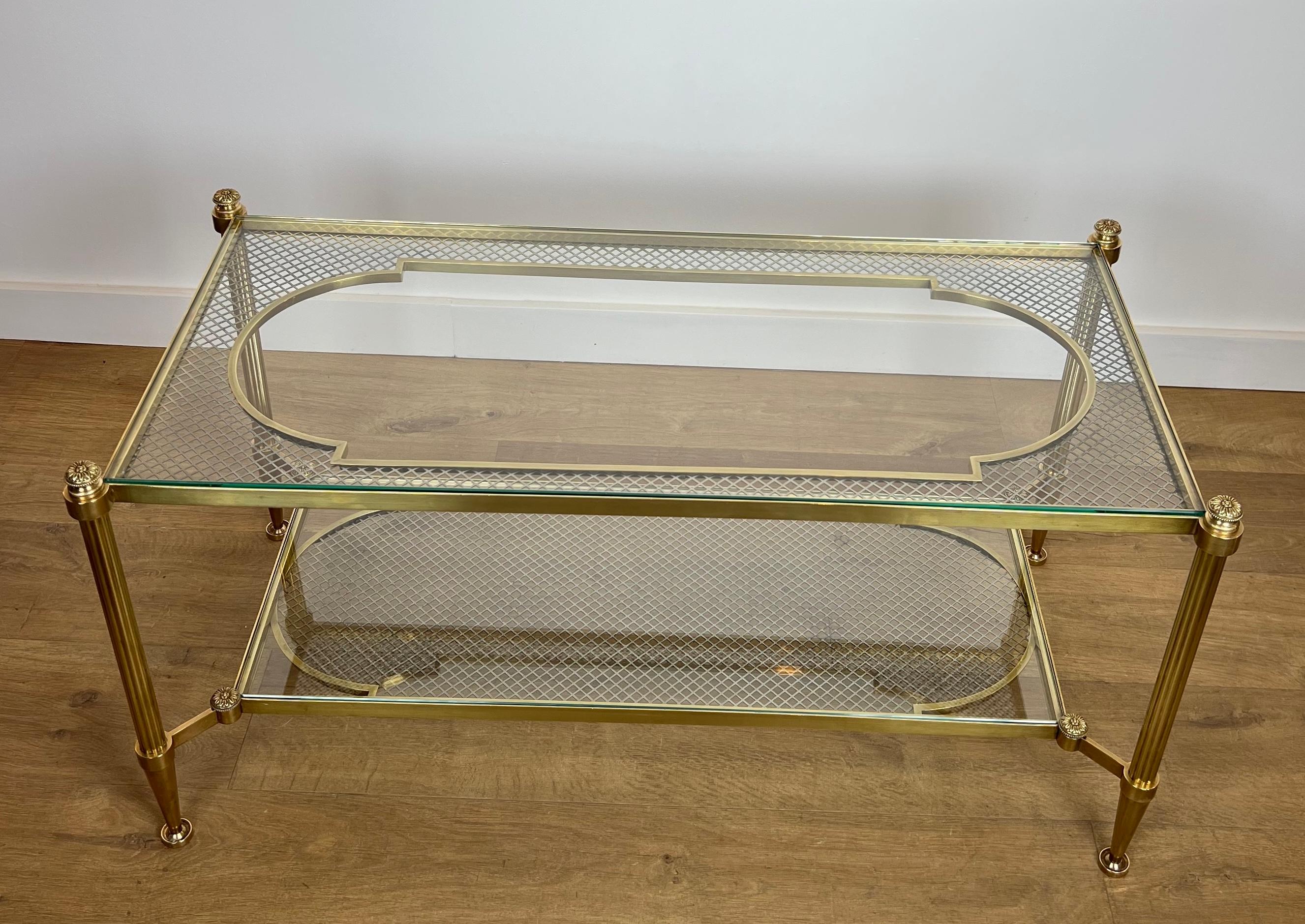 This rare and exceptional coffee table is made of bronze, brass and steel with two tiers glass top resting on a steel mesh. The upper plate offers a pattern repeated in reverse for the lower plate. Fluted feet are topped with a bronze element