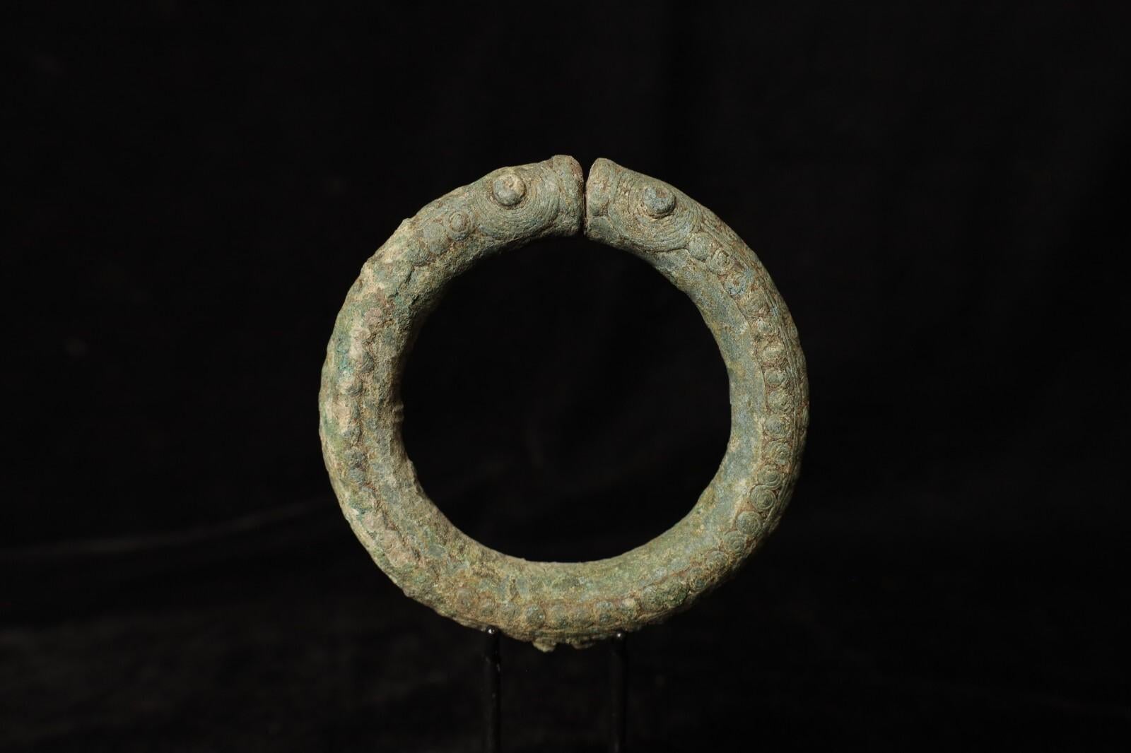 An exceptional and rare Bronze Age bangle from ancient Thailand, cast in the form of two stylized serpents facing one another — a motif rich in symbolic meaning across early Southeast Asian cultures. This striking piece is beautifully patinated, the