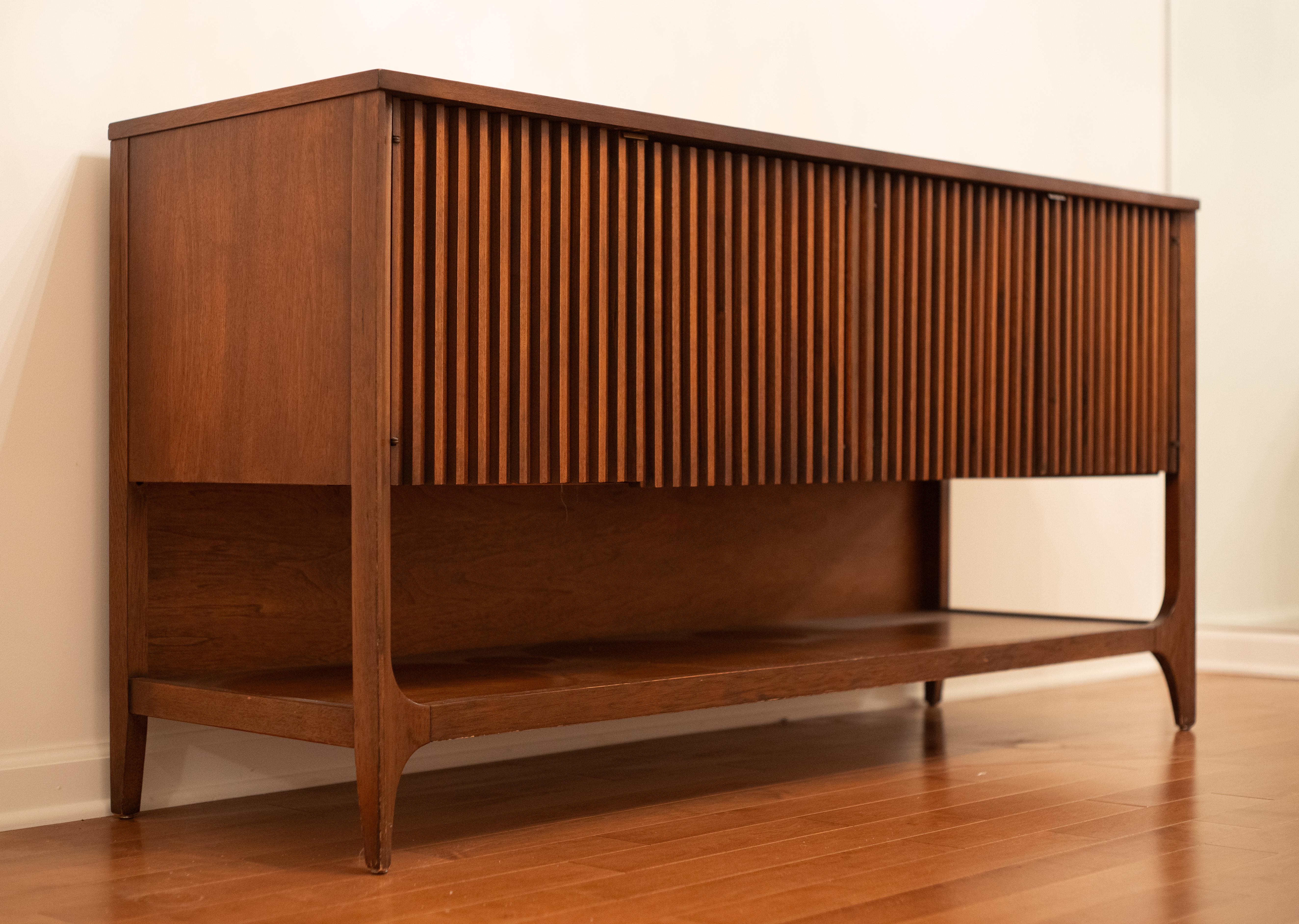 Designed and made in the United States, this model is one of many in the Brasilia line. This one, however, is more special than most. It features four fluted carved walnut doors, which open to reveal three large drawers on the right and two shelves