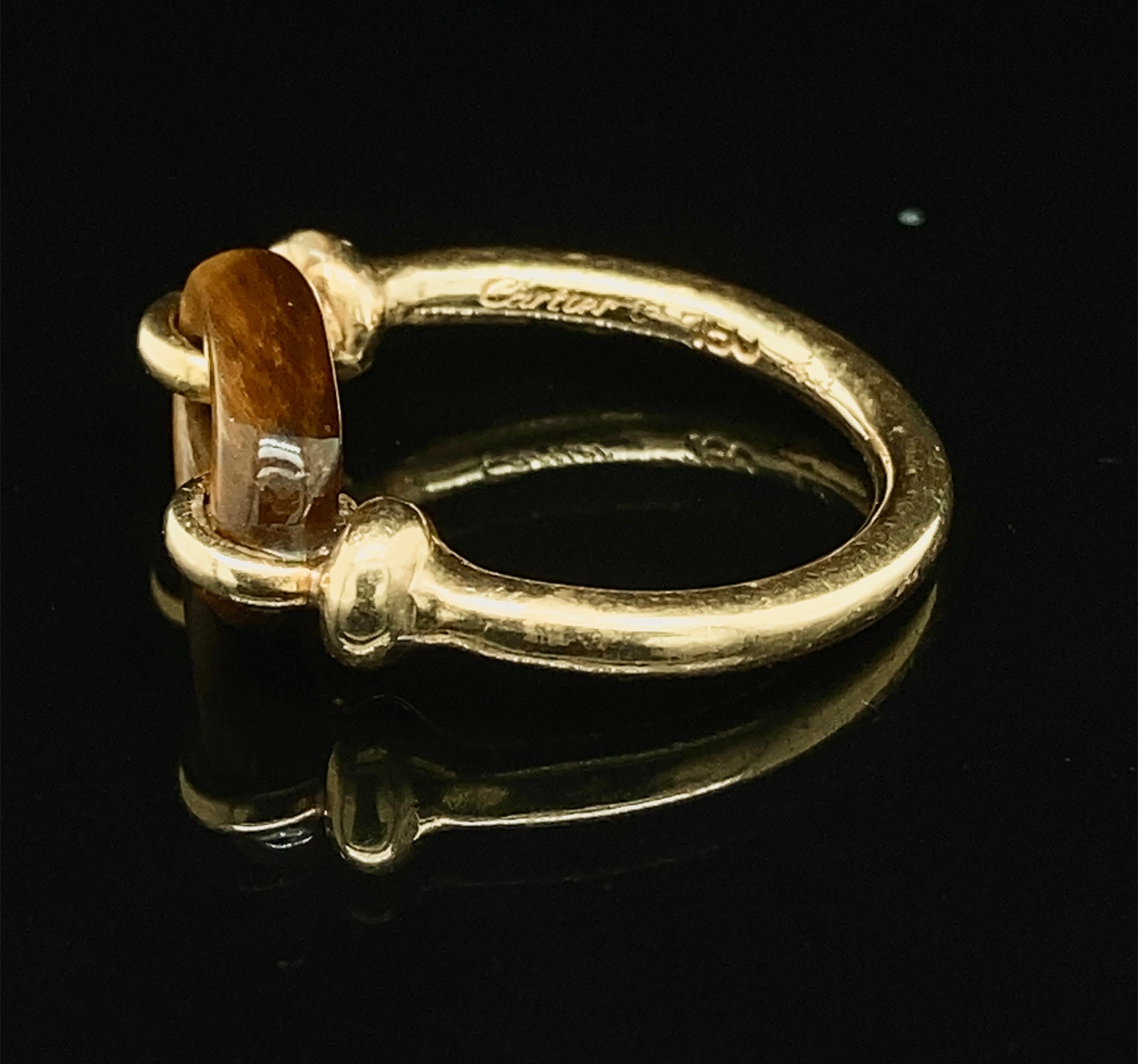 A delicate 18K gold Cartier ring, the tiger's eye carved in a loop, held within the gold ring, 
signed and numbered Cartier 54329 and marked 750, 
ring size 4 3/4, I,
4 g.
In good overall condition with beautiful shimmer to the tiger's eye.
