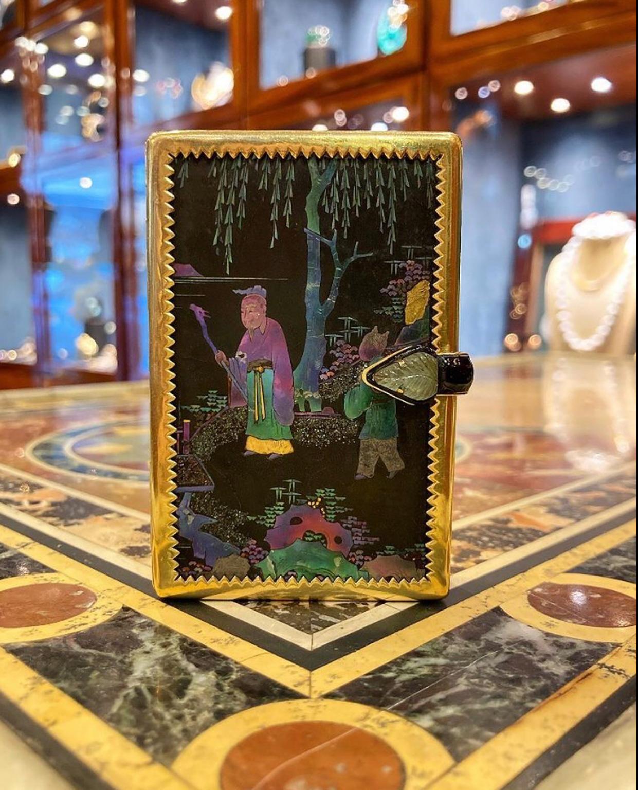 A rare collectible Art Deco Cartier lacque burgauté vanity case featuring a carved emerald and onyx thumb piece. It depicts an Eastern scene in iridescent mother of pearl, accented by diamonds on the reverse and coral pillars at the sides. Made in