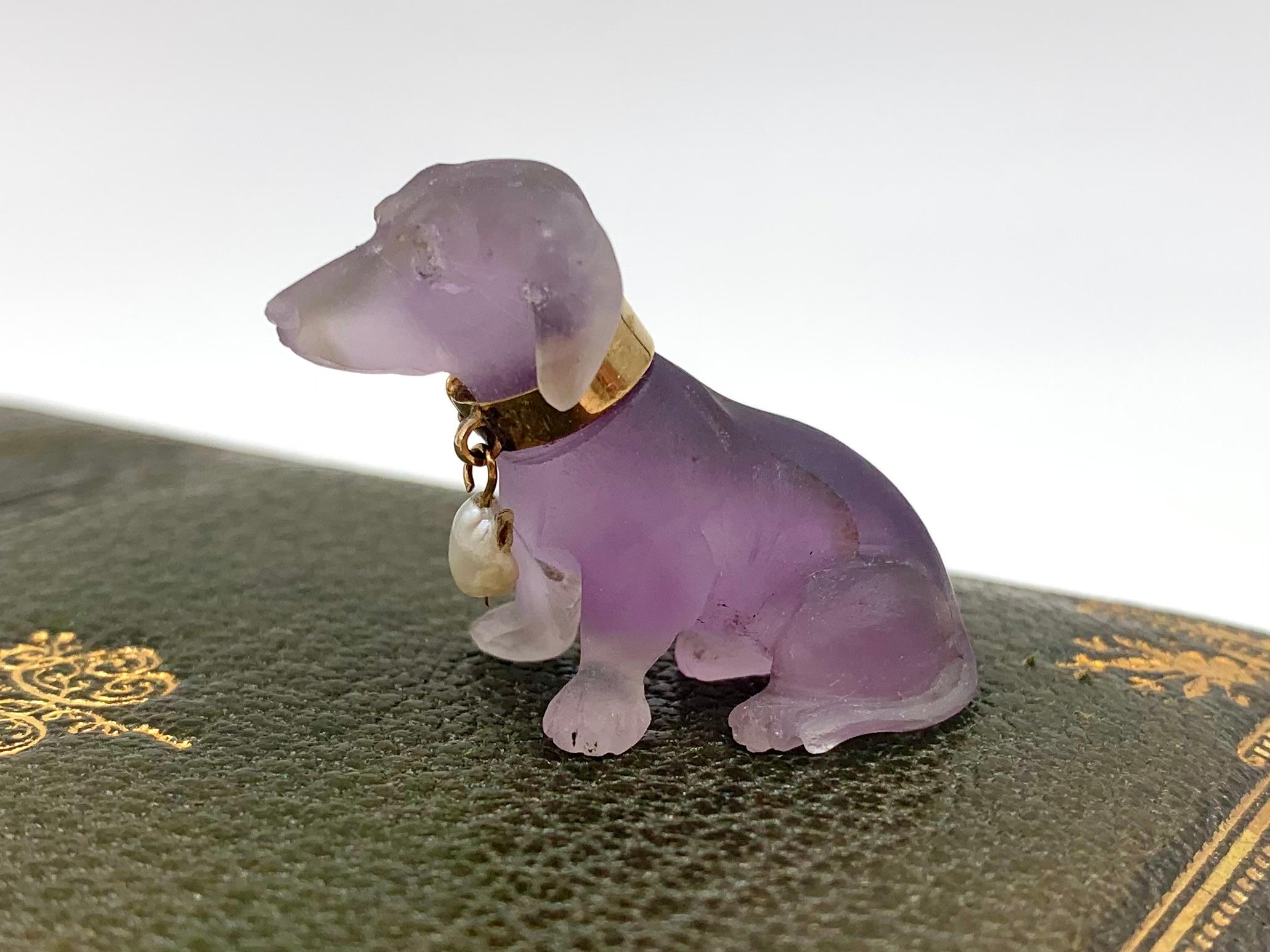 Wunderschöner geschnitzter Amethyst, Diamant, natürliche Perle 18K Gelbgold Dackel
Anfang des 20. Jahrhunderts
Naturgetreu modellierter, attraktiver Farbverlauf des Amethysts, Diamantaugen, Hundehalsband aus 18 Karat Gelbgold mit einem Anhänger aus