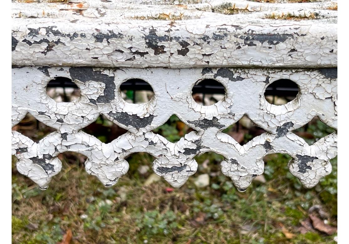  A white paint decorated cast iron curtain settee with tripartite back panels displaying c-scrolls and s-scrolls, arabesque pattern, ornamental crests with fleur di lis atop back panels, decorative aprons at the seat edge and resting upon four legs