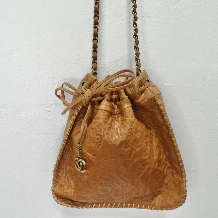 Stunning brown leather Chanel drawstring handbag circa 2011! Brown leather is embossed with iconic Chanel camellias which gives this bag such an elegant touch. Featuring brass hardware, a brass and interwoven leather crossbody style chain as the