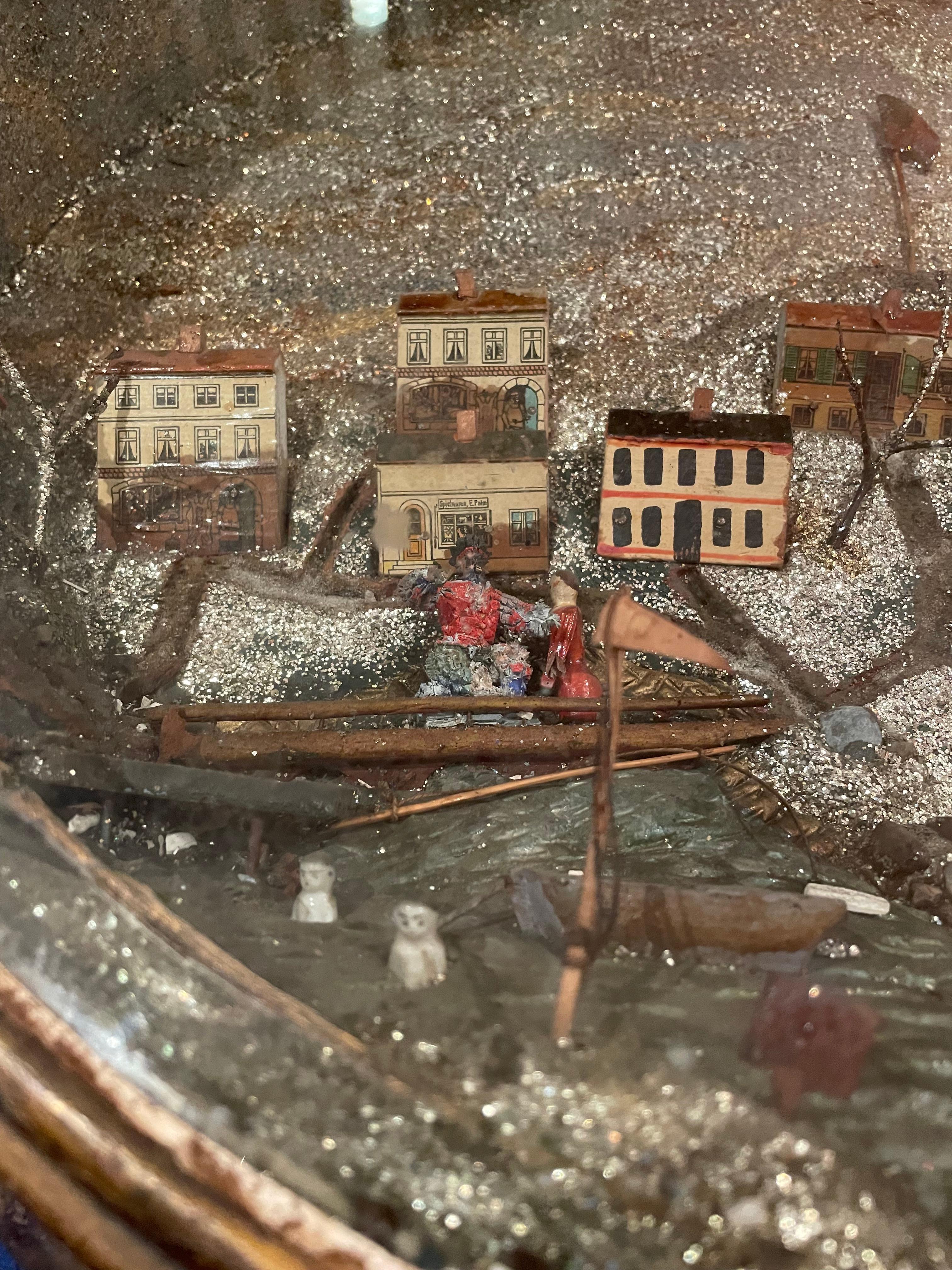 A very unique 19th century folk art diorama depicting a seaside townscape with a glitter background and sky. The diorama includes boaters, a hunter, swimmers, a windmill and homes in a village. The creator of this piece of folk art paid particular