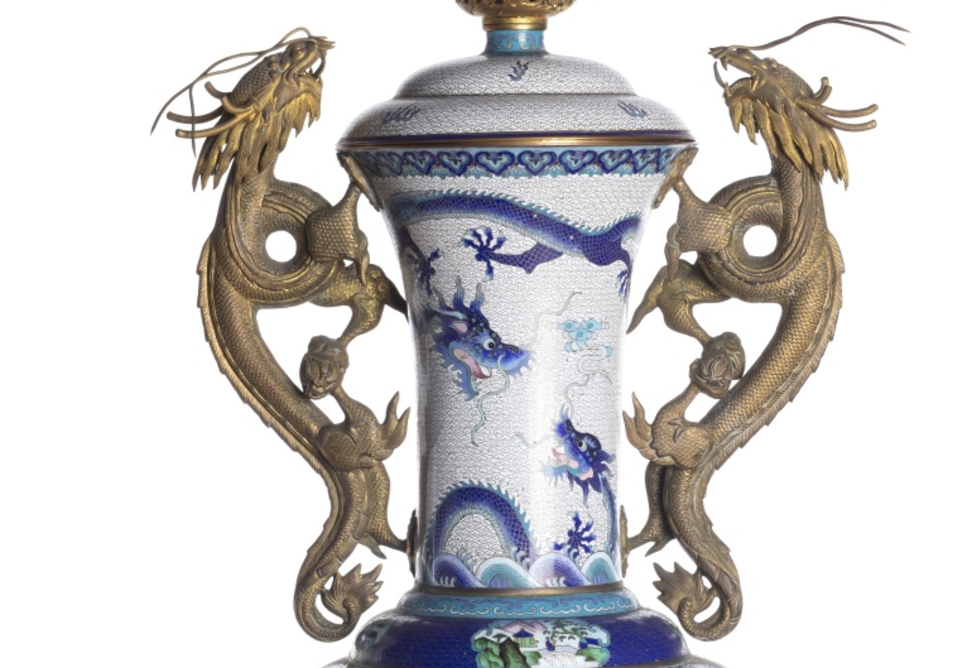 TOPF MIT DECKEL

Chinesisch
 19. Jahrhundert,
 in Cloisonné-Metall, Dekoration in Blautönen und Polychromie mit Drachen und drachenförmigen Griffen in Reliefbronze. 
Sockel aus Holz. 
Höhe: (Vase) 61 cm. Höhe: (insgesamt) 70 cm.
sehr guter