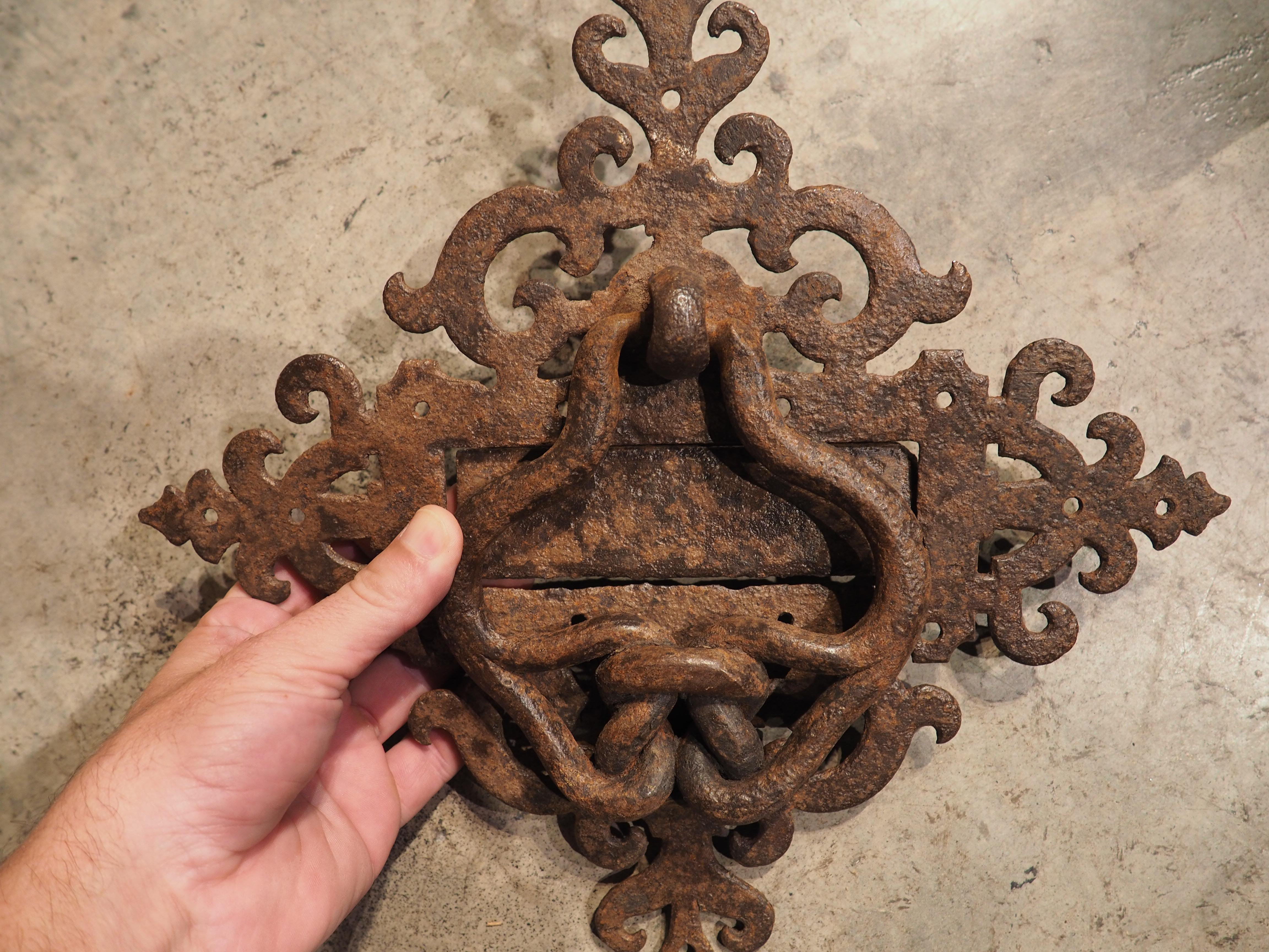 This wrought iron door knocker has a rare size and intricate design with a flap designed to be a peephole or possibly for deliveries of letters. Hand-crafted in France, circa 1700, the knocker has developed a fantastic patina due to oxidation from