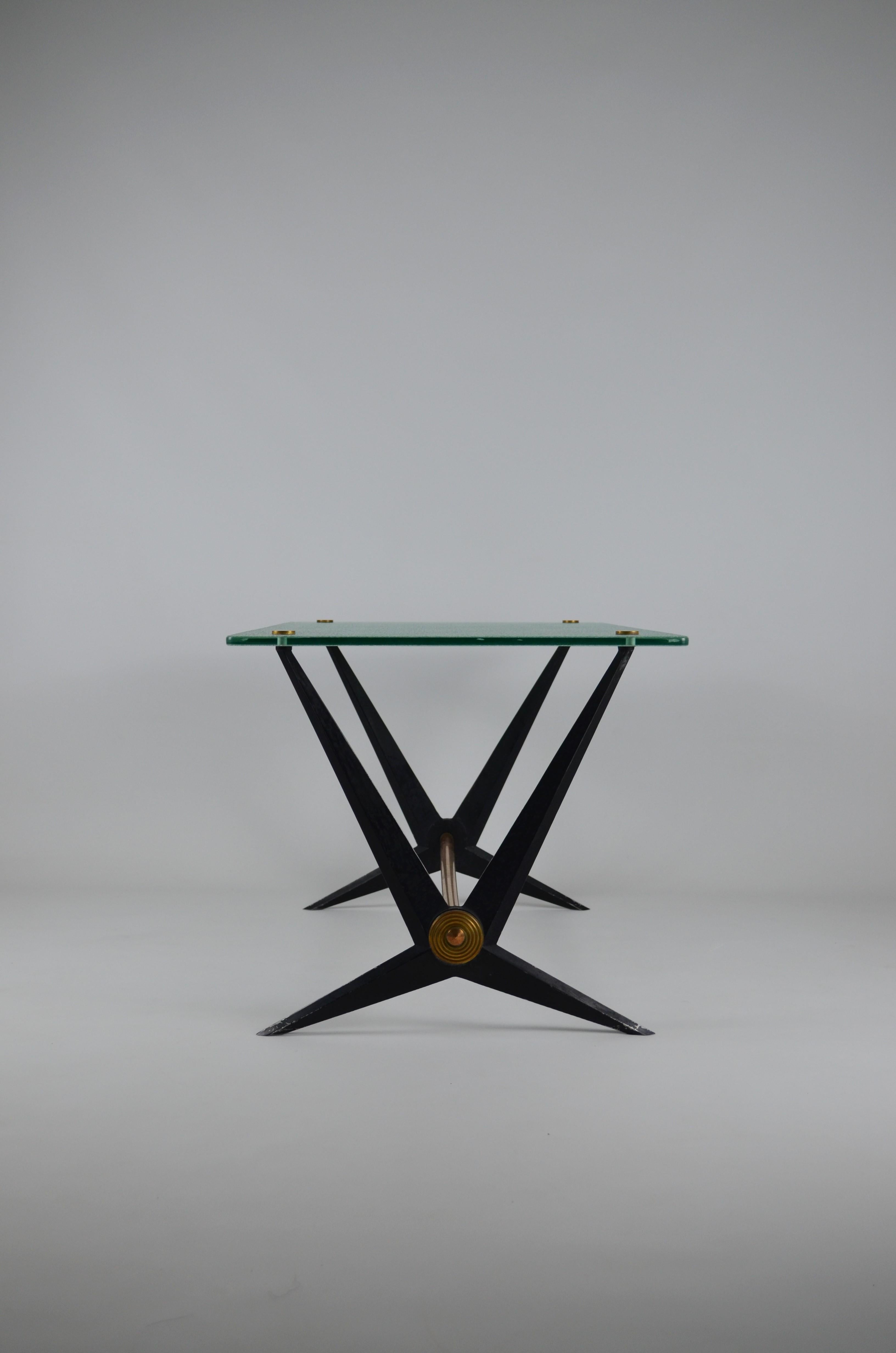 Very elegant coffee table by Angelo Ostuni, 1950s.
It is composed of an angular black enameled metal frame with brass embellishments.
Attached glass top is pierced and capped with four round brass caps.
The table is totally original (no